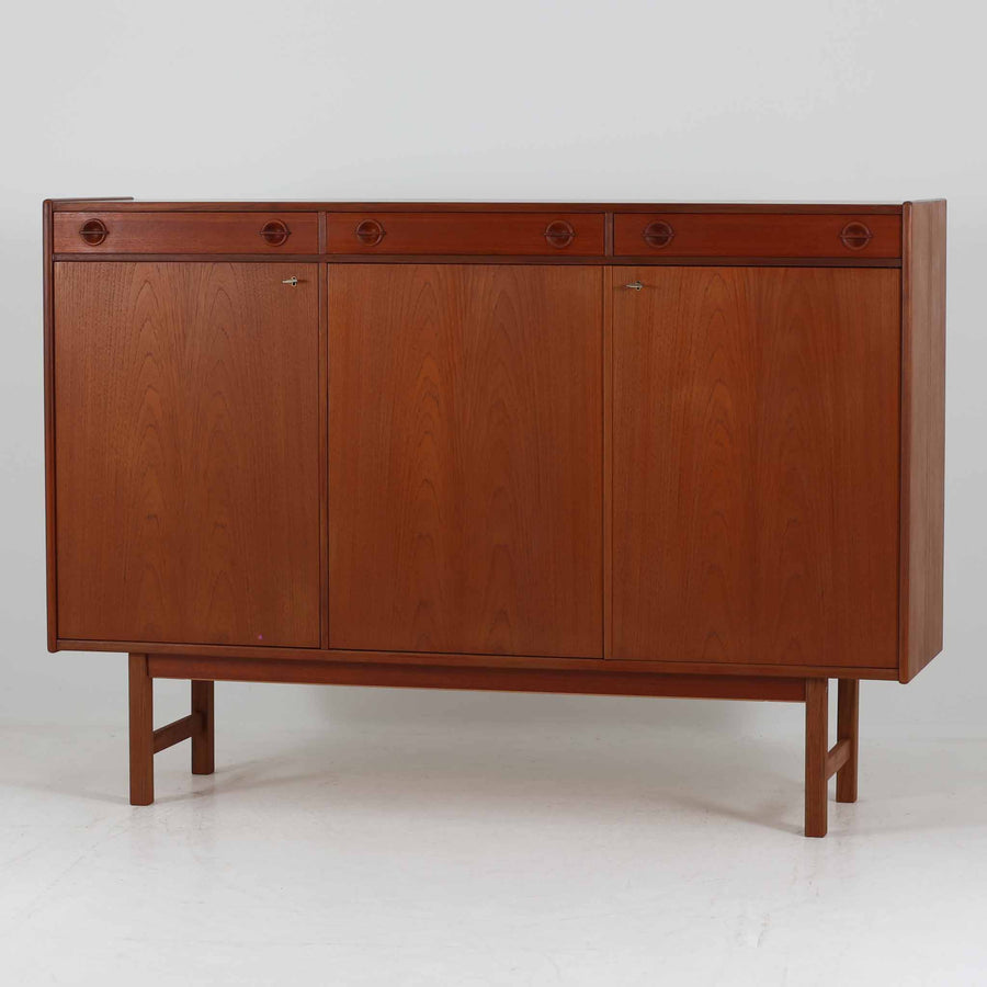 Tage Olofsson（ターゲ・オロフソン）によるデザインで、Ulferts Mobler社製のキッチンキャビネットです。チーク材を贅沢に使用した美しい木目と、丸型の引き手がアクセントとなったデザインが特徴です。上部にはカトラリーなどを整理できる仕切り付きの引き出しが3杯、下部には棚板付きの扉収納が備えられており、食器やキッチン用品を効率的に収納できます。北欧家具らしい温もりと機能性を兼ね備えた一台で、リビングやダイニングにも自然に溶け込む上品な佇まいです。