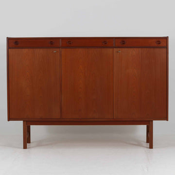 Tage Olofsson（ターゲ・オロフソン）によるデザインで、Ulferts Mobler社製のキッチンキャビネットです。チーク材を贅沢に使用した美しい木目と、丸型の引き手がアクセントとなったデザインが特徴です。上部にはカトラリーなどを整理できる仕切り付きの引き出しが3杯、下部には棚板付きの扉収納が備えられており、食器やキッチン用品を効率的に収納できます。北欧家具らしい温もりと機能性を兼ね備えた一台で、リビングやダイニングにも自然に溶け込む上品な佇まいです。