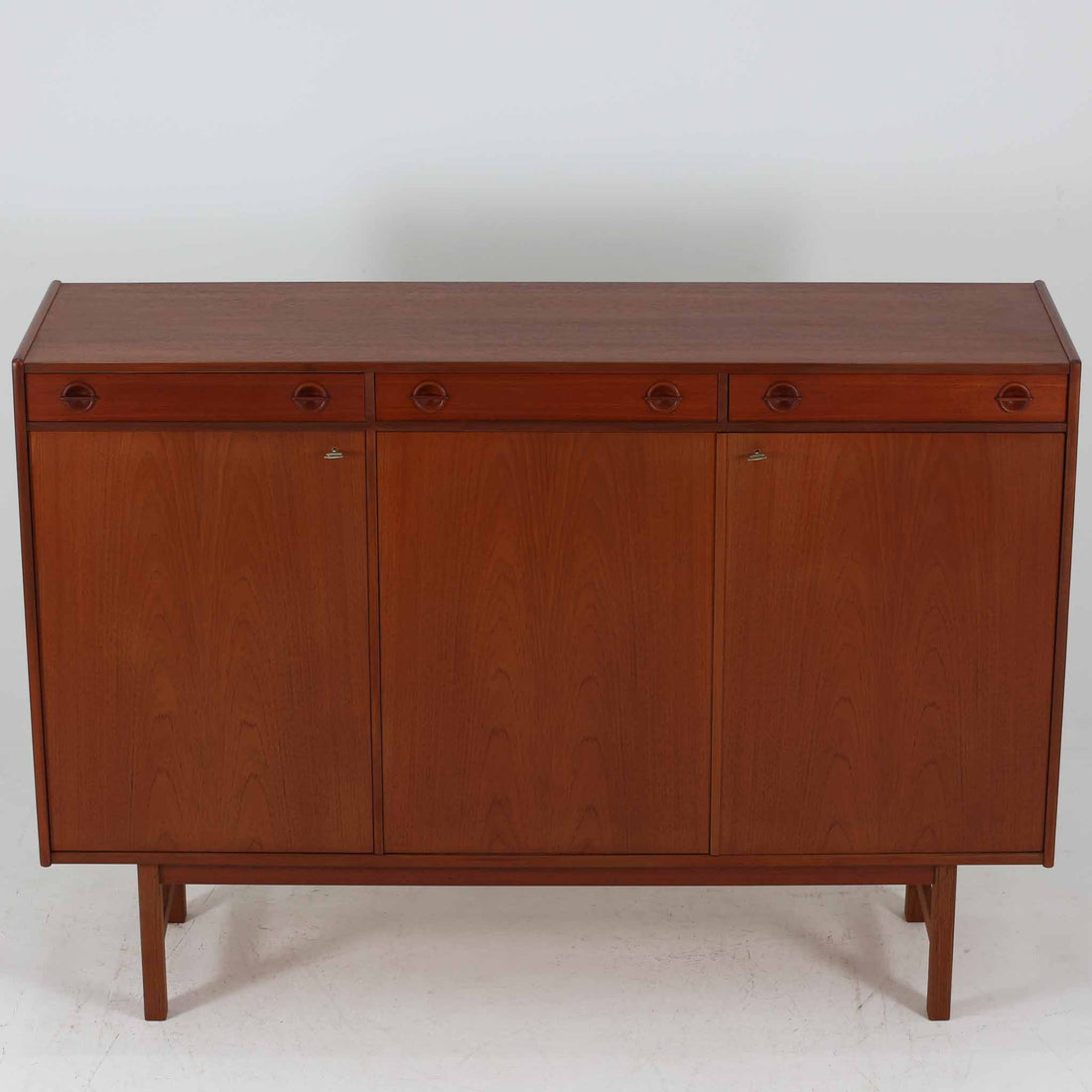 Tage Olofsson（ターゲ・オロフソン）によるデザインで、Ulferts Mobler社製のキッチンキャビネットです。チーク材を贅沢に使用した美しい木目と、丸型の引き手がアクセントとなったデザインが特徴です。上部にはカトラリーなどを整理できる仕切り付きの引き出しが3杯、下部には棚板付きの扉収納が備えられており、食器やキッチン用品を効率的に収納できます。北欧家具らしい温もりと機能性を兼ね備えた一台で、リビングやダイニングにも自然に溶け込む上品な佇まいです。