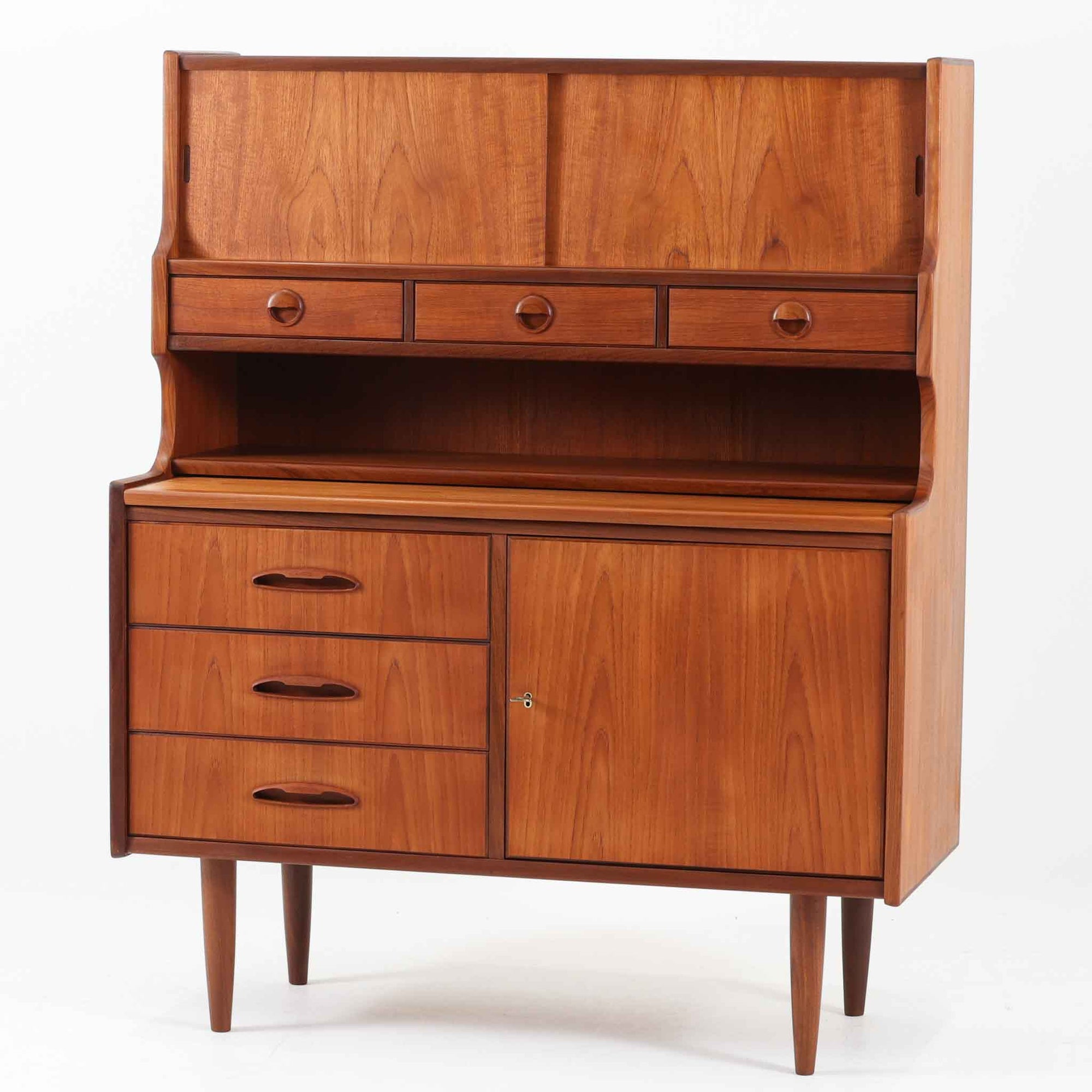 デンマーク製のビンテージライティングビューロです。チーク材を使用した温かみのある木肌と美しい木目が印象的で、北欧家具ならではの上質な存在感を放ちます。上部の引き戸収納や小引き出し、下部の引き出しとキャビネットを備え、機能的に整理できる実用的な設計が魅力。天板をデスクとして使えるため、書き物や作業スペースとしても活躍します。丸みを帯びたフォルムや細身の脚部が軽やかな印象を与え、経年により深みを増したチークの風合いがビンテージ家具ならではの味わいを楽しめる一台です。