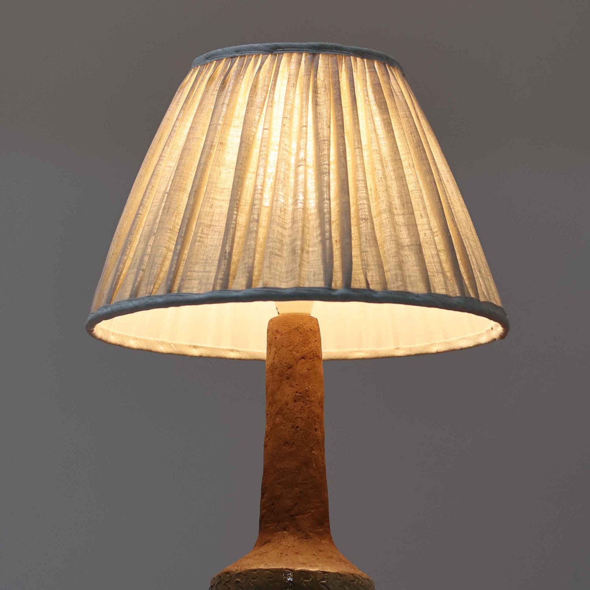 デンマーク製のテーブルランプは、高さ50cmと存在感のあるサイズが魅力の一点物ビンテージ品です。陶磁器ベースは下部に緑がかった釉薬を施し、上部は素地を生かしたマットな質感で仕上げられており、素材のコントラストがデザインの個性を際立たせています。プリーツ入りのリネンシェードを透す光はやわらかく広がり、リビングや寝室を温かみのある雰囲気に演出します。メーカー不詳・デザイナー不明ながら、Studio Potteryらしいクラフトマンシップを感じられる一点物の北欧ビンテージ品です。