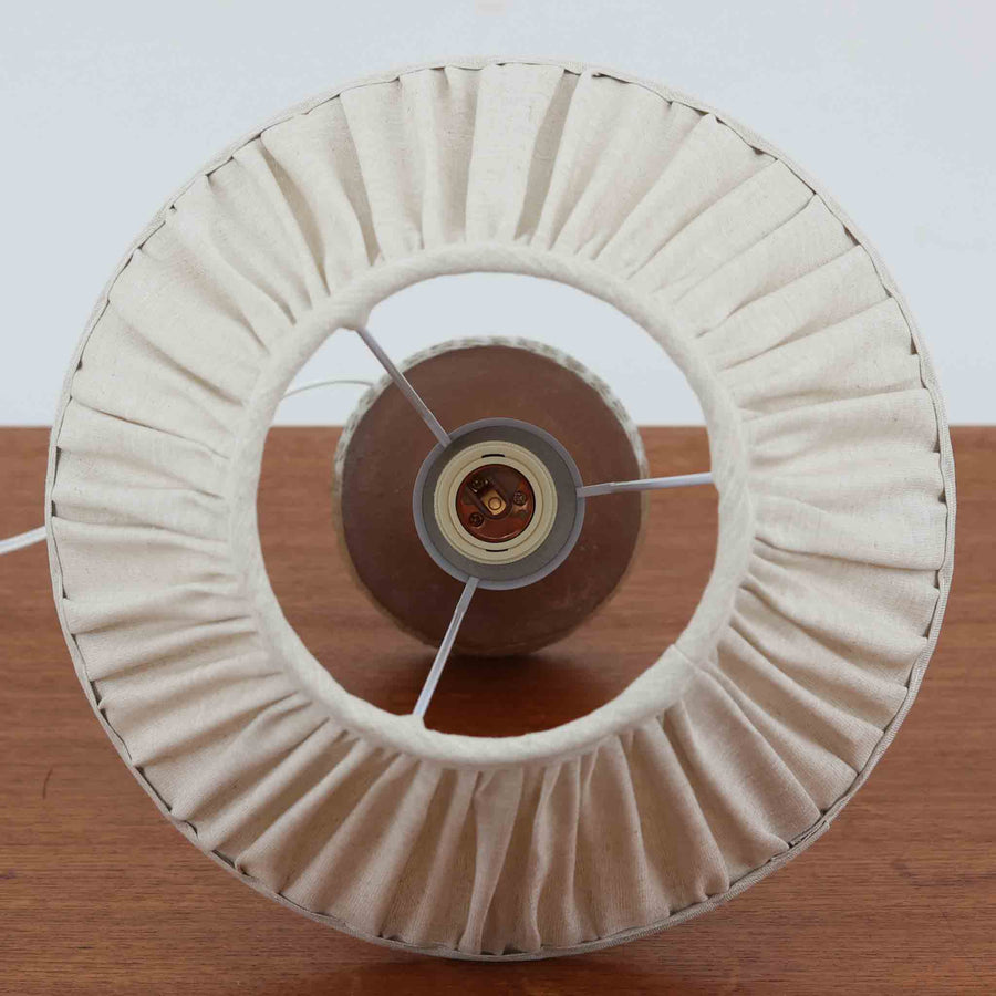 デンマーク製のテーブルランプは、高さ50cmと存在感のあるサイズが魅力の一点物ビンテージ品です。陶磁器ベースは下部に緑がかった釉薬を施し、上部は素地を生かしたマットな質感で仕上げられており、素材のコントラストがデザインの個性を際立たせています。プリーツ入りのリネンシェードを透す光はやわらかく広がり、リビングや寝室を温かみのある雰囲気に演出します。メーカー不詳・デザイナー不明ながら、Studio Potteryらしいクラフトマンシップを感じられる一点物の北欧ビンテージ品です。