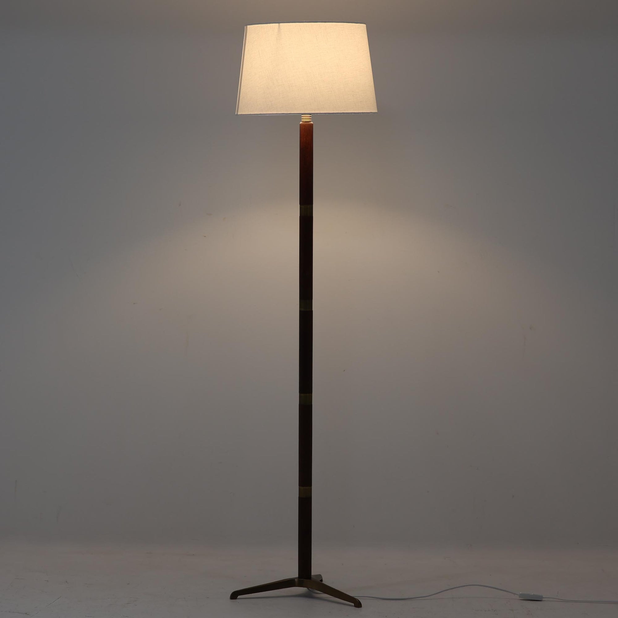 デンマーク製のフロアランプで、洗練された北欧デザインの魅力が詰まった一品です。高さ136cmのスマートなフォルムに、温かみのあるチーク材と真鍮のコンビネーションが美しく調和し、落ち着いた雰囲気を演出します。リネンシェードから広がる柔らかな光は、リビングや寝室を心地よい空間に変えてくれます。脚部の真鍮ベースは安定感があり、経年による素材の風合いがビンテージならではの魅力を一層引き立てています。シンプルながら存在感のある佇まいで、上質なインテリアにふさわしい照明です。