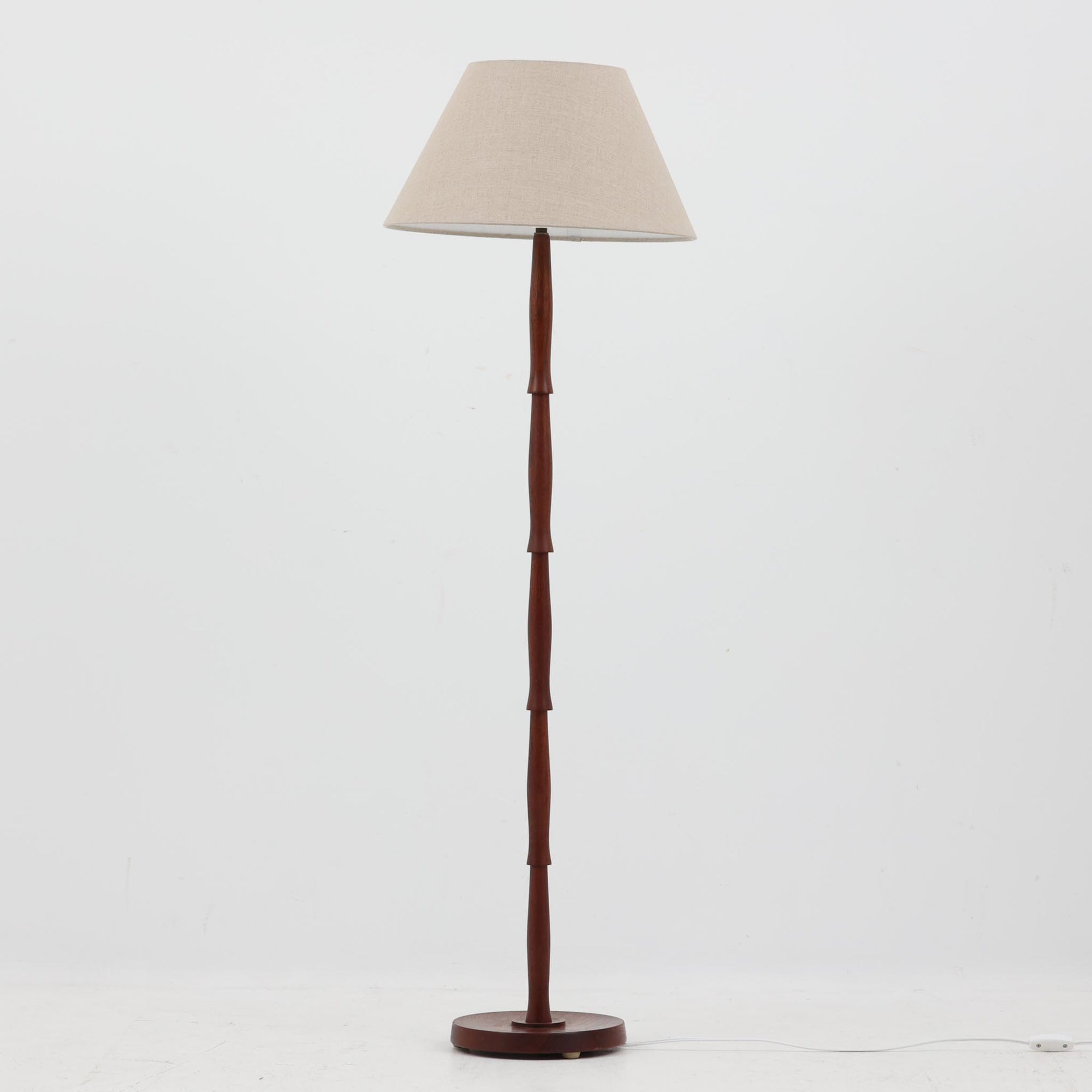 高さ125cmのデンマーク製フロアランプです。支柱にはチーク材が用いられ、滑らかな曲線を描く削り出しのディテールが温かみのある北欧デザインを際立たせています。ベース部分は安定感があり、真鍮パーツがアクセントとなり上品な雰囲気を演出。リネンシェードを通した柔らかな光が、リビングや寝室を心地よい空間へと導きます。素材の経年変化による深みや風合いも魅力で、ナチュラルで落ち着いた北欧ビンテージの存在感を楽しめる一品です。