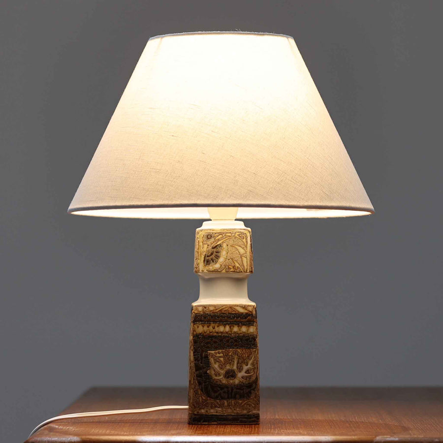 Nils Thorssonがデザインし、Royal Copenhagen社から発表された「BACA」シリーズのテーブルランプは、高さ38cmのバランスの取れたサイズ感で、北欧ビンテージらしい存在感を放ちます。陶磁器製のベースには細やかな装飾模様が施され、グラフィカルでありながら落ち着いた色調が空間に洗練された雰囲気を添えます。リネンシェードを透過する柔らかな光が温もりを演出し、リビングやベッドサイドに最適です。年月を経て深みを増した質感と工芸的な美しさを楽しめる一点物です。
