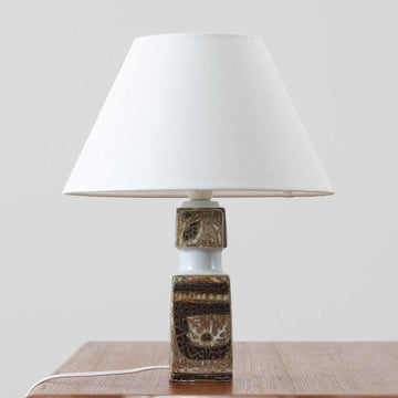 Nils Thorssonがデザインし、Royal Copenhagen社から発表された「BACA」シリーズのテーブルランプは、高さ38cmのバランスの取れたサイズ感で、北欧ビンテージらしい存在感を放ちます。陶磁器製のベースには細やかな装飾模様が施され、グラフィカルでありながら落ち着いた色調が空間に洗練された雰囲気を添えます。リネンシェードを透過する柔らかな光が温もりを演出し、リビングやベッドサイドに最適です。年月を経て深みを増した質感と工芸的な美しさを楽しめる一点物です。