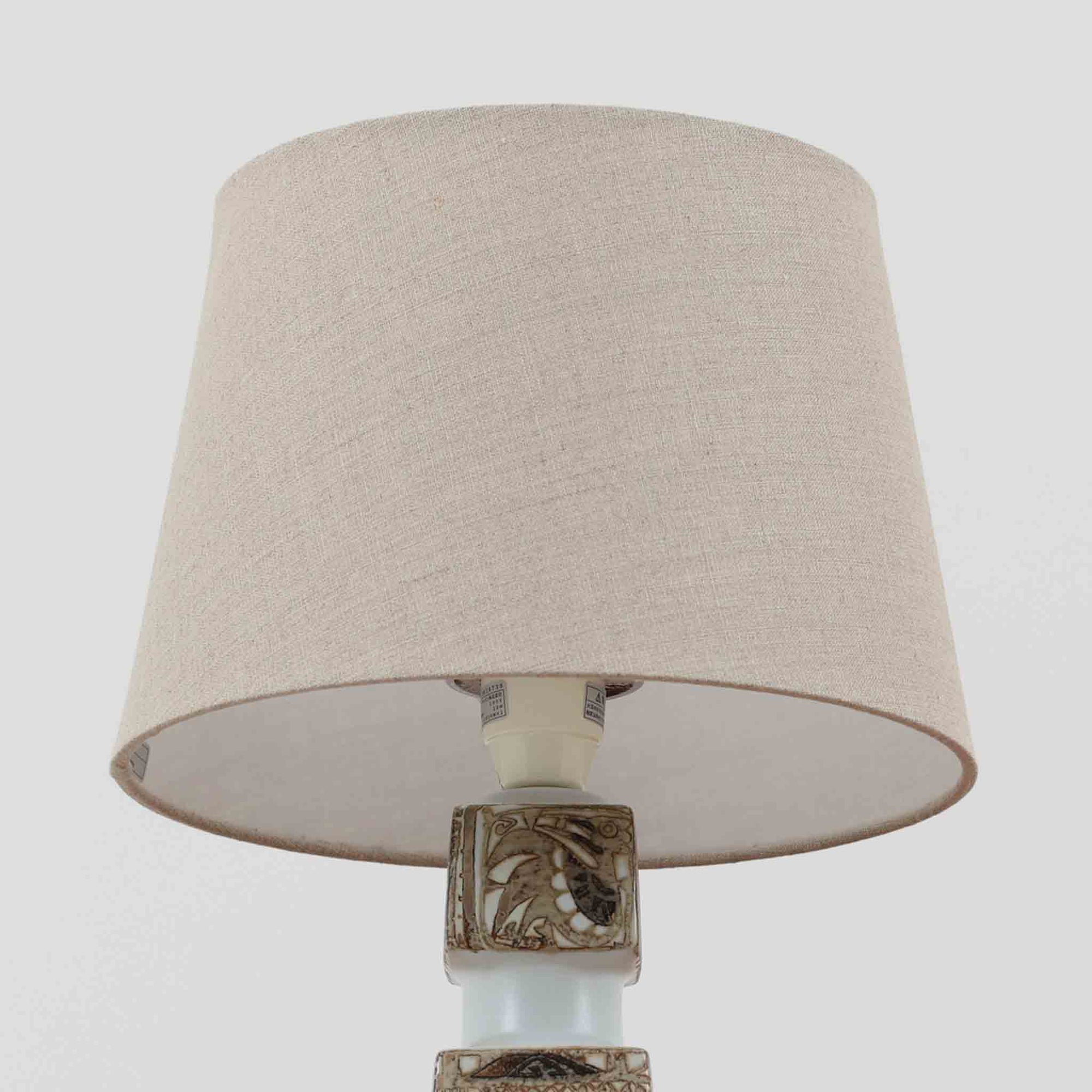 Nils Thorssonがデザインし、Royal Copenhagen社から発表された「BACA」シリーズのテーブルランプは、高さ39cmのバランスの取れたサイズ感で、北欧ビンテージらしい存在感を放ちます。陶磁器製のベースには細やかな装飾模様が施され、グラフィカルでありながら落ち着いた色調が空間に洗練された雰囲気を添えます。リネンシェードを透過する柔らかな光が温もりを演出し、リビングやベッドサイドに最適です。年月を経て深みを増した質感と工芸的な美しさを楽しめる一点物です。