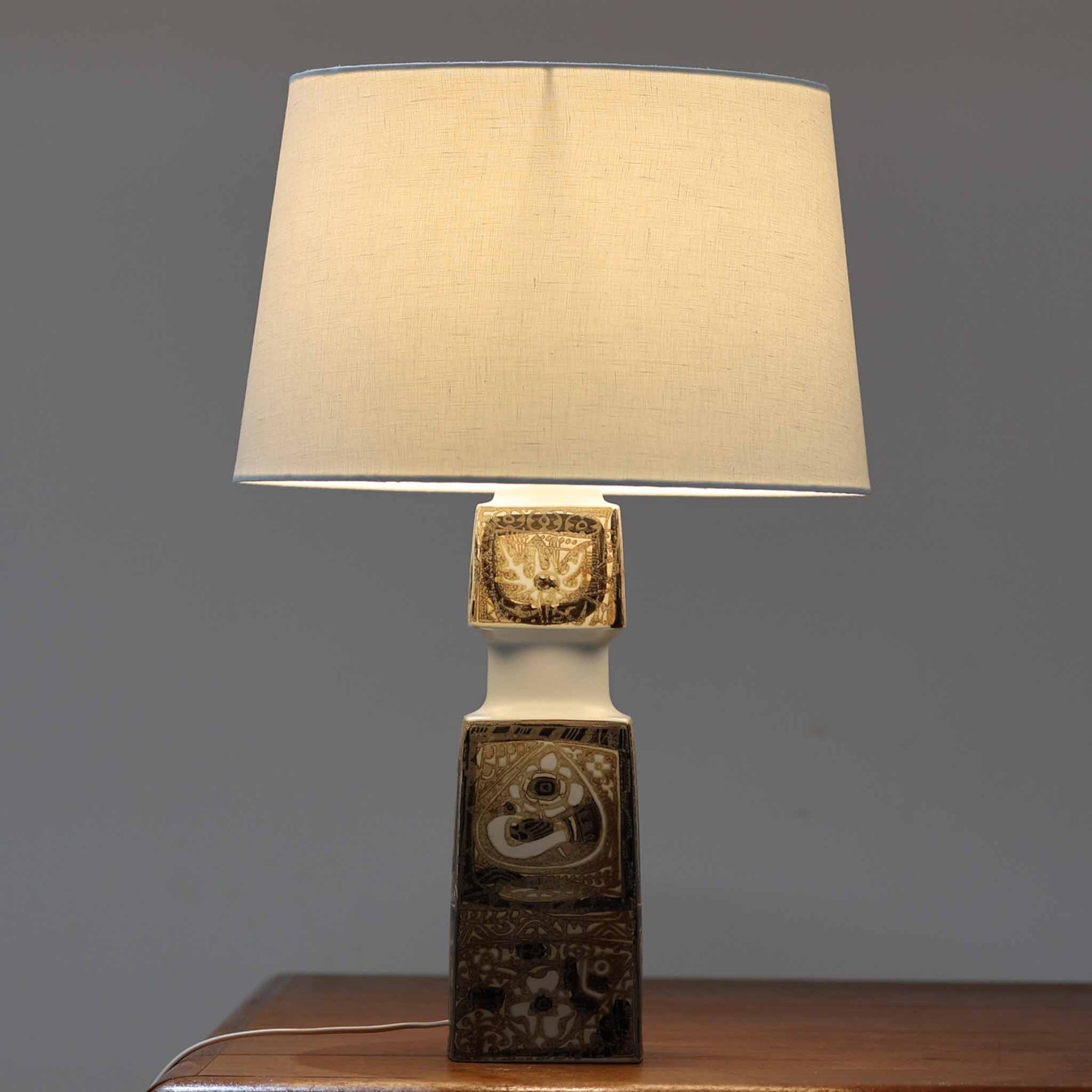 Nils Thorssonがデザインし、Royal Copenhagen社から発表されたBACAシリーズのこちらのテーブルランプは、高さ50cmと大きめのサイズで空間に存在感を放ちます。陶磁器製のベースにはトールソンならではの幾何学的かつ装飾的なパターンが施され、芸術性とクラフト感が融合した独特の魅力を漂わせています。リネンシェードを通した柔らかな光はリビングやベッドサイドに落ち着きをもたらし、ビンテージならではの経年の深みが一点物としての価値を高めています。