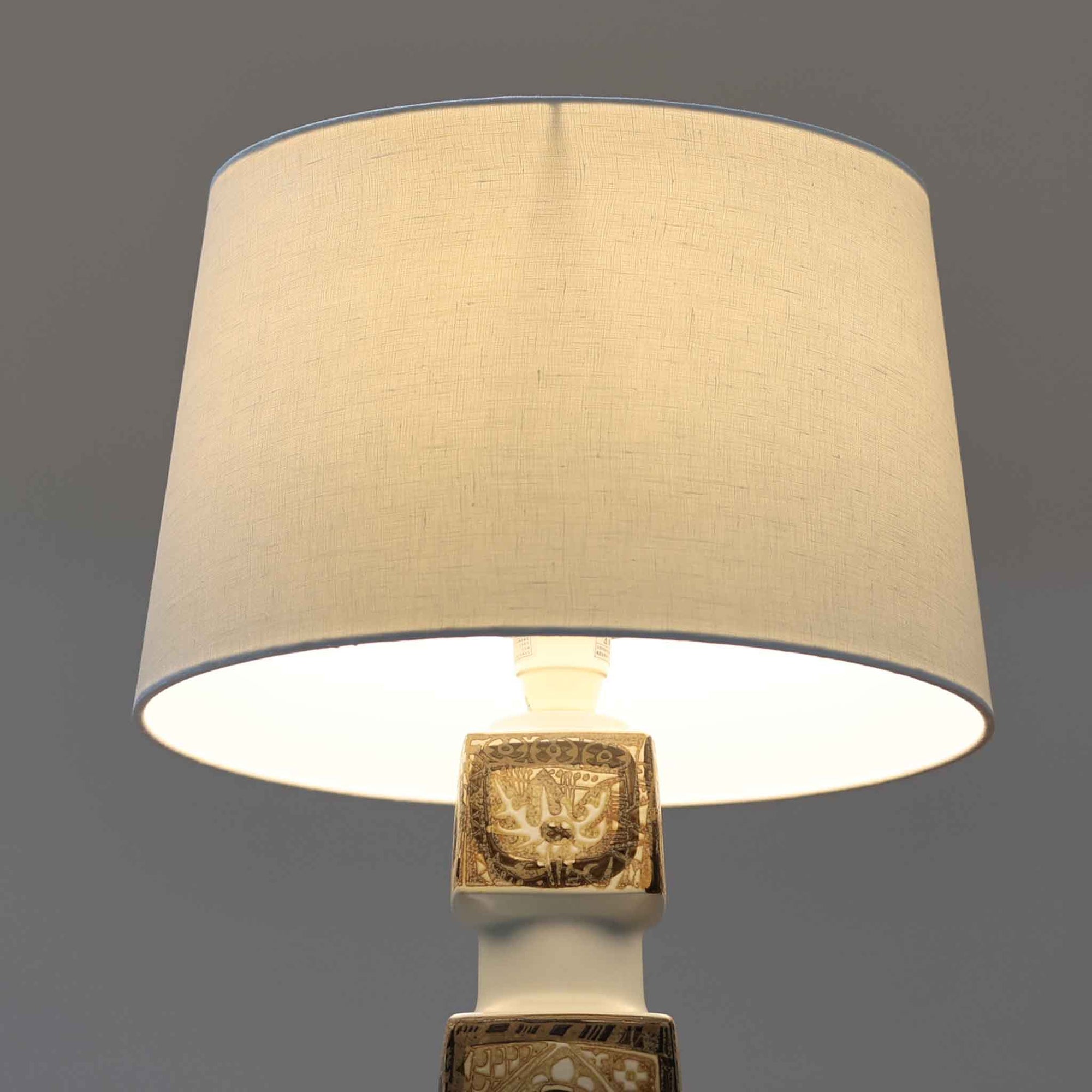 Nils Thorssonがデザインし、Royal Copenhagen社から発表されたBACAシリーズのこちらのテーブルランプは、高さ50cmと大きめのサイズで空間に存在感を放ちます。陶磁器製のベースにはトールソンならではの幾何学的かつ装飾的なパターンが施され、芸術性とクラフト感が融合した独特の魅力を漂わせています。リネンシェードを通した柔らかな光はリビングやベッドサイドに落ち着きをもたらし、ビンテージならではの経年の深みが一点物としての価値を高めています。