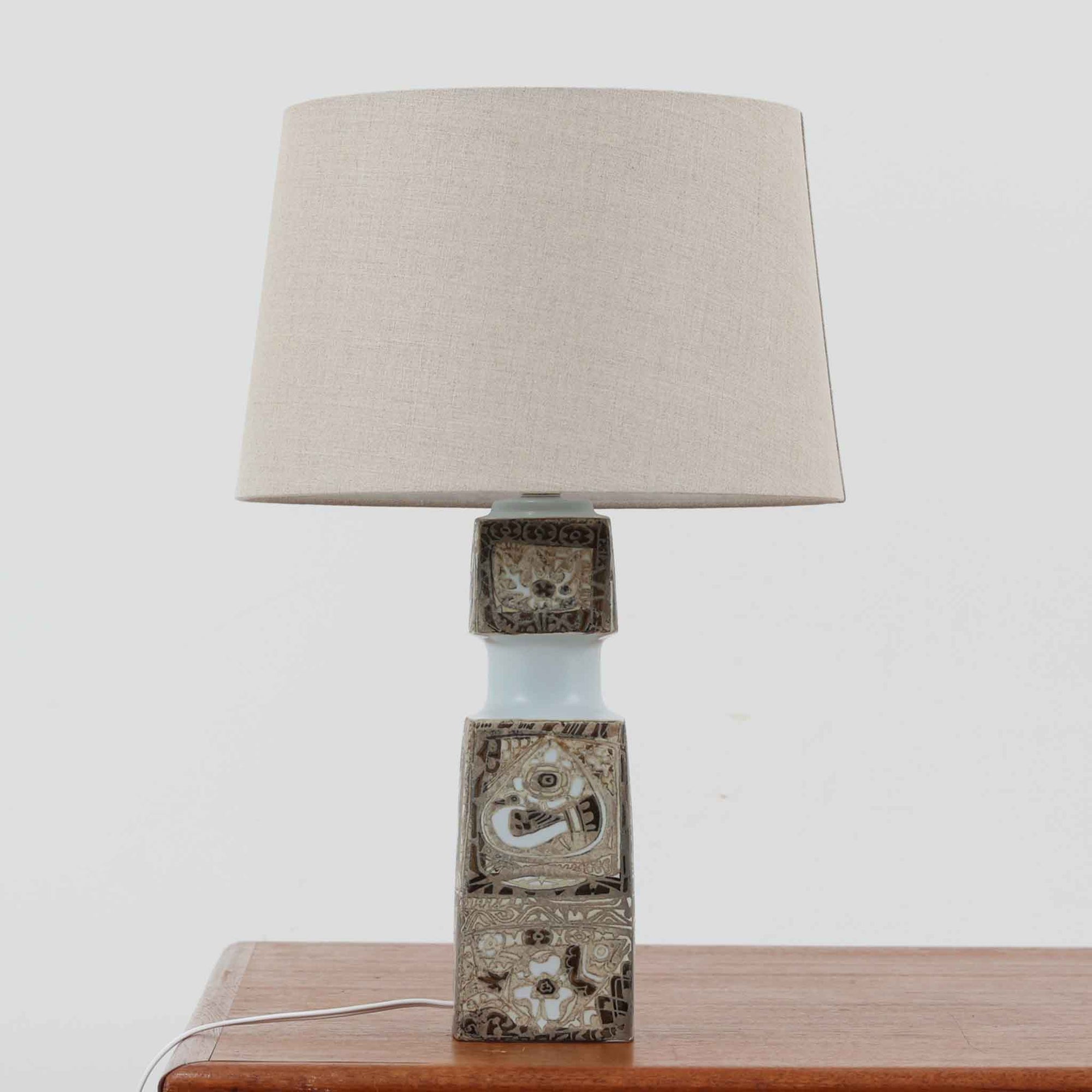 Nils ThorssonによるRoyal Copenhagen社のBACAシリーズのテーブルランプは、高さ50cmと大ぶりで存在感のあるビンテージアイテムです。陶磁器のベースにはトールソンらしい細密な装飾パターンが施され、幾何学的でありながら有機的なモチーフが調和し、芸術性を感じさせます。リネンシェードを透す光は柔らかく広がり、リビングや寝室を温かく包み込みます。年月を経た釉薬の風合いとクラフト感が、北欧ビンテージならではの魅力を引き立てる逸品です。