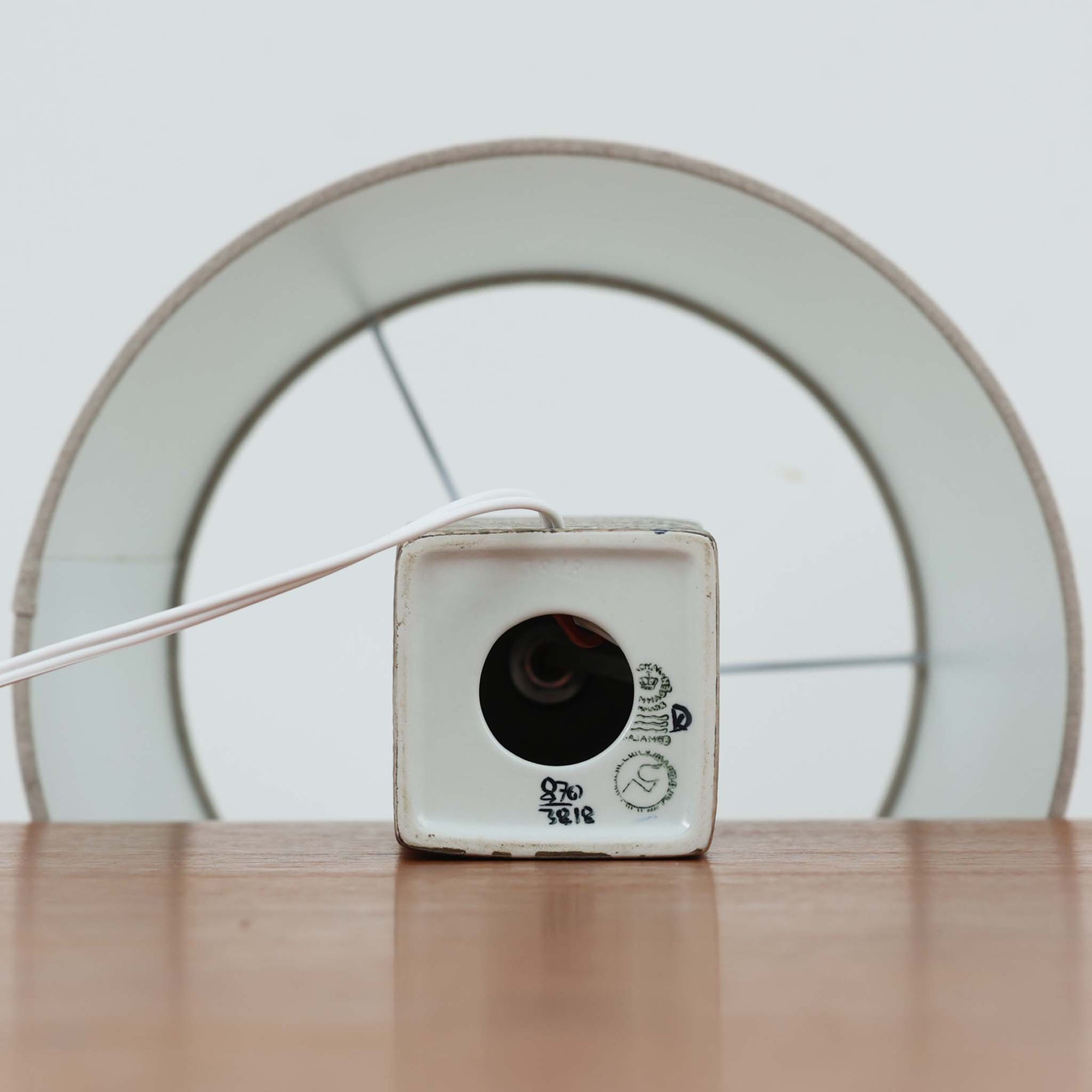 Nils Thorssonが手掛けたRoyal Copenhagen社BACAシリーズのテーブルランプは、高さ41cmの程よいサイズ感で空間に上質な存在感を与えます。陶磁器のベースには幾何学的で抽象的なモチーフが施され、複雑な釉薬の表情が芸術性を引き立てています。シンプルなリネンシェードを透した光は柔らかく広がり、リビングやベッドサイドを温かみのある雰囲気に演出。クラフトマンシップとデザイン性が融合した北欧ビンテージの魅力を存分に味わえる逸品です。