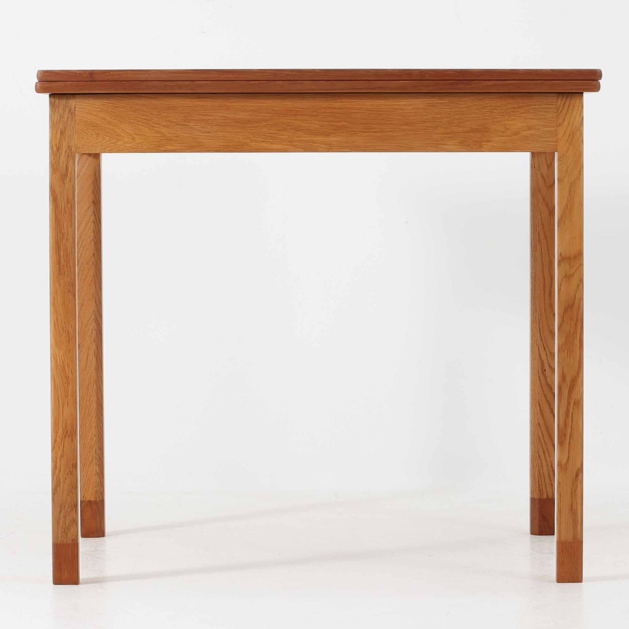 Borge Mogensen（ボーエ・モーエンセン）がSoborgのために手掛けた「Folding table」は、チーク材の天板とオーク材の脚部を組み合わせた温かみある佇まいが魅力のダイニングテーブルで、中央の蝶番を開閉して幅80～120cmへと柔軟に調整できる構造が特徴です。内部にはモーエンセン家具らしい実用性を備えた収納スペースが設けられ、ゲームテーブルとして親しまれてきた背景を感じさせます。経年により深まった木肌の風合いがビンテージならではの味わいをまとい、ダイニングやワークスペースのサブテーブルとしても多用途に活躍する一台です。また、裏面には「SKM」の刻印が確認でき、スウェーデン軍（Svenska KrigsMakten）の備品として使用されていたことを示しています。