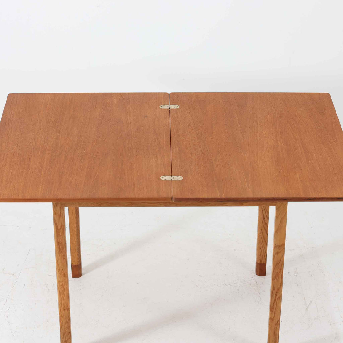 Borge Mogensen（ボーエ・モーエンセン）がSoborgのために手掛けた「Folding table」は、チーク材の天板とオーク材の脚部を組み合わせた温かみある佇まいが魅力のダイニングテーブルで、中央の蝶番を開閉して幅80～120cmへと柔軟に調整できる構造が特徴です。内部にはモーエンセン家具らしい実用性を備えた収納スペースが設けられ、ゲームテーブルとして親しまれてきた背景を感じさせます。経年により深まった木肌の風合いがビンテージならではの味わいをまとい、ダイニングやワークスペースのサブテーブルとしても多用途に活躍する一台です。また、裏面には「SKM」の刻印が確認でき、スウェーデン軍（Svenska KrigsMakten）の備品として使用されていたことを示しています。