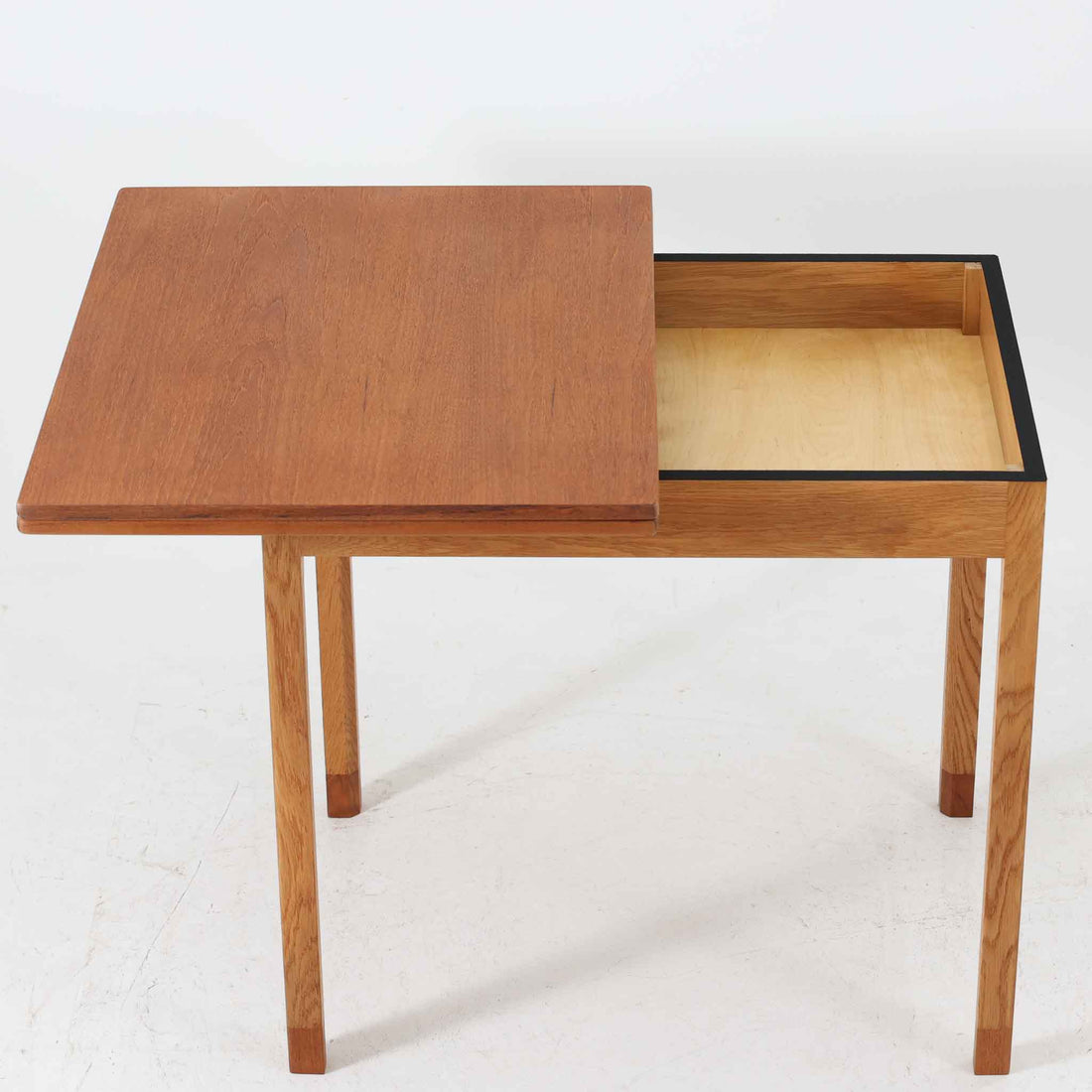 Borge Mogensen（ボーエ・モーエンセン）がSoborgのために手掛けた「Folding table」は、チーク材の天板とオーク材の脚部を組み合わせた温かみある佇まいが魅力のダイニングテーブルで、中央の蝶番を開閉して幅80～120cmへと柔軟に調整できる構造が特徴です。内部にはモーエンセン家具らしい実用性を備えた収納スペースが設けられ、ゲームテーブルとして親しまれてきた背景を感じさせます。経年により深まった木肌の風合いがビンテージならではの味わいをまとい、ダイニングやワークスペースのサブテーブルとしても多用途に活躍する一台です。また、裏面には「SKM」の刻印が確認でき、スウェーデン軍（Svenska KrigsMakten）の備品として使用されていたことを示しています。