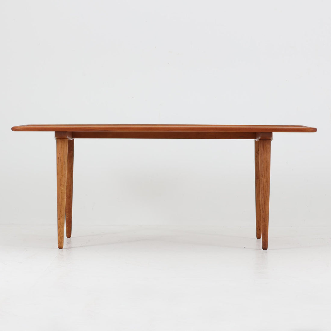 Hans J. Wegner（ハンス・J・ウェグナー）によるAndreas Tuck社製のセンターテーブル「AT11」です。幅130cmの広々とした天板はチーク無垢材を使用し、縁には繊細な面取り加工が施され、柔らかな印象を与えます。脚部には堅牢なオーク無垢材が用いられ、軽やかなテーパードデザインが北欧家具らしいバランスの良さを感じさせます。さらに脚のネジ部分まで木製で仕上げられており、細部に至るまで職人技が光る逸品です。脚は取り外し可能な構造で、輸送や設置も容易です。シンプルでありながら素材の美しさが際立ち、経年変化による深みを増した木肌がビンテージならではの存在感を放ちます。リビングの中心に置いて使うことで、空間に上質な雰囲気を添える一台です。