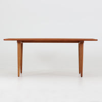 Hans J. Wegner（ハンス・J・ウェグナー）によるAndreas Tuck社製のセンターテーブル「AT11」です。幅130cmの広々とした天板はチーク無垢材を使用し、縁には繊細な面取り加工が施され、柔らかな印象を与えます。脚部には堅牢なオーク無垢材が用いられ、軽やかなテーパードデザインが北欧家具らしいバランスの良さを感じさせます。さらに脚のネジ部分まで木製で仕上げられており、細部に至るまで職人技が光る逸品です。脚は取り外し可能な構造で、輸送や設置も容易です。シンプルでありながら素材の美しさが際立ち、経年変化による深みを増した木肌がビンテージならではの存在感を放ちます。リビングの中心に置いて使うことで、空間に上質な雰囲気を添える一台です。