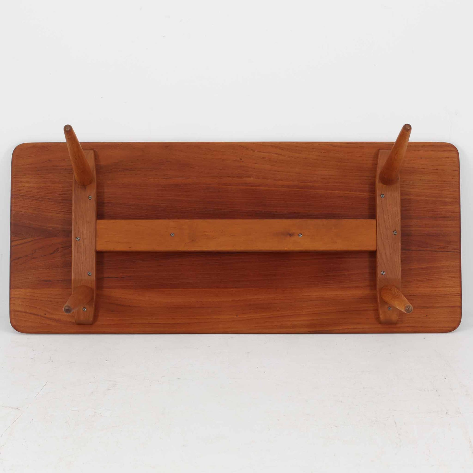 Hans J. Wegner（ハンス・J・ウェグナー）によるAndreas Tuck社製のセンターテーブル「AT11」です。幅130cmの広々とした天板はチーク無垢材を使用し、縁には繊細な面取り加工が施され、柔らかな印象を与えます。脚部には堅牢なオーク無垢材が用いられ、軽やかなテーパードデザインが北欧家具らしいバランスの良さを感じさせます。さらに脚のネジ部分まで木製で仕上げられており、細部に至るまで職人技が光る逸品です。脚は取り外し可能な構造で、輸送や設置も容易です。シンプルでありながら素材の美しさが際立ち、経年変化による深みを増した木肌がビンテージならではの存在感を放ちます。リビングの中心に置いて使うことで、空間に上質な雰囲気を添える一台です。