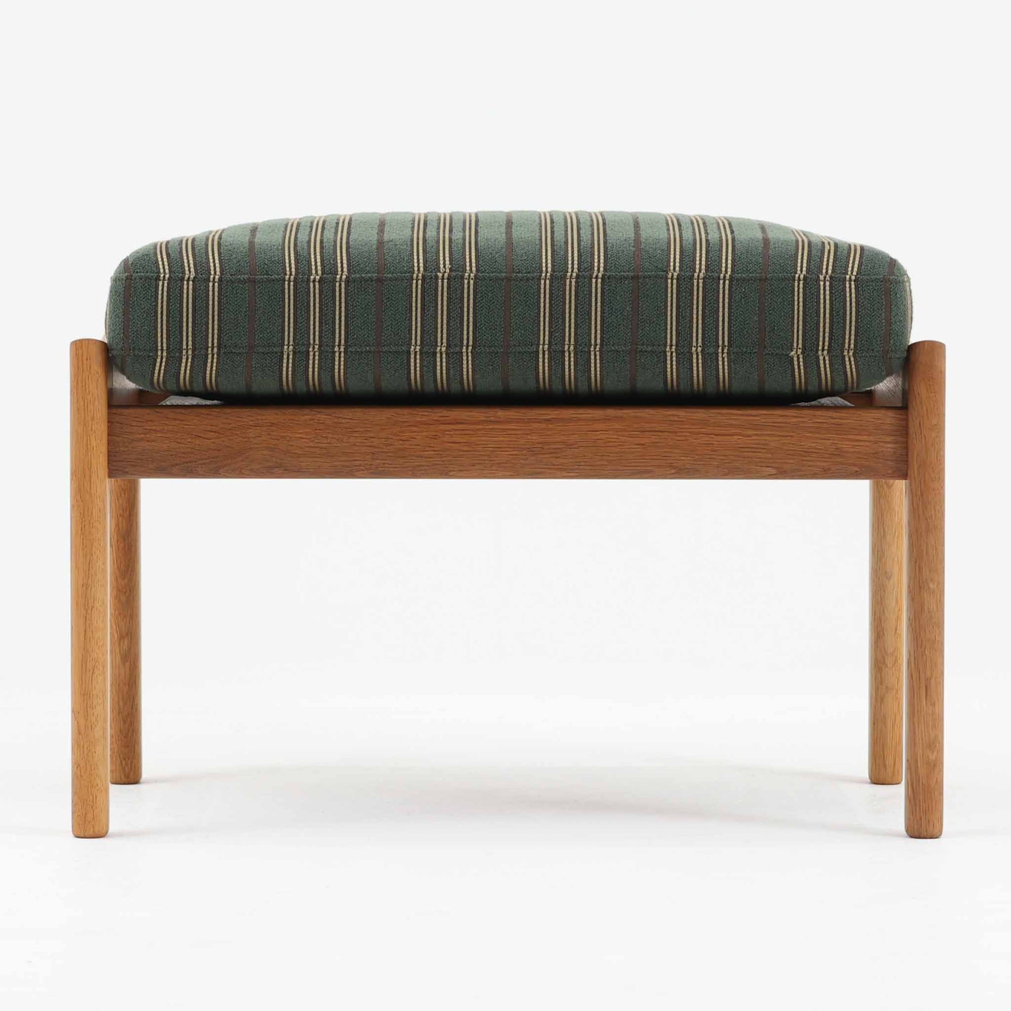 Hans J. Wegnerがデザインし、Getamaが製作したGE290オットマンの希少なサイドテーブル兼用タイプです。オーク材の美しい木目を活かしたフレームは、丸みを帯びたアーム状の意匠が印象的で、安定感のある堅牢な構造が魅力。クッションを外せばトレーテーブルとしても使用できる実用的な設計です。本品はGetama社の刻印が入る以前の古いタイプで、初期モデルならではの佇まいも価値を高めています。ラウンジチェアと合わせてはもちろん、単体でも存在感を放つ北欧ビンテージの逸品です。クッション内部にはビンテージ品ならではのスプリングが内包されています。