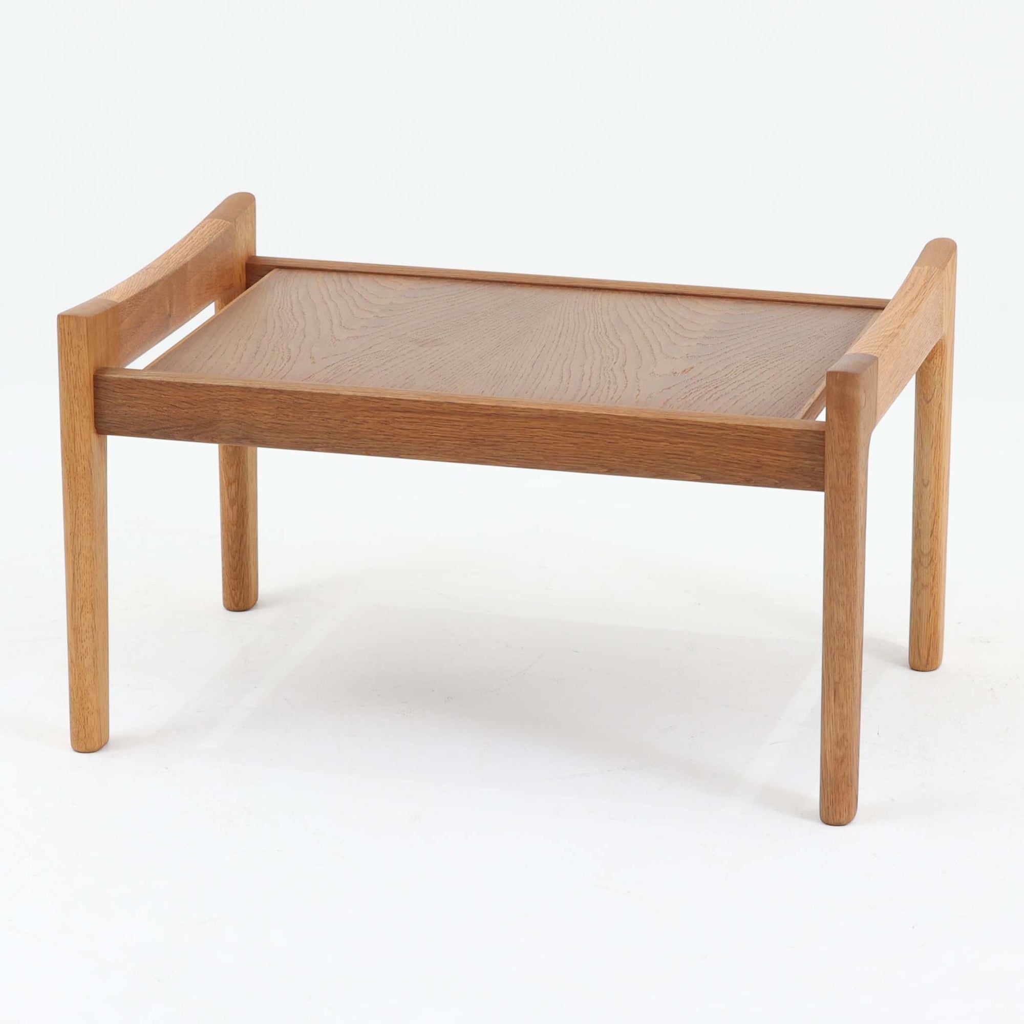 Hans J. Wegnerがデザインし、Getamaが製作したGE290オットマンの希少なサイドテーブル兼用タイプです。オーク材の美しい木目を活かしたフレームは、丸みを帯びたアーム状の意匠が印象的で、安定感のある堅牢な構造が魅力。クッションを外せばトレーテーブルとしても使用できる実用的な設計です。本品はGetama社の刻印が入る以前の古いタイプで、初期モデルならではの佇まいも価値を高めています。ラウンジチェアと合わせてはもちろん、単体でも存在感を放つ北欧ビンテージの逸品です。クッション内部にはビンテージ品ならではのスプリングが内包されています。