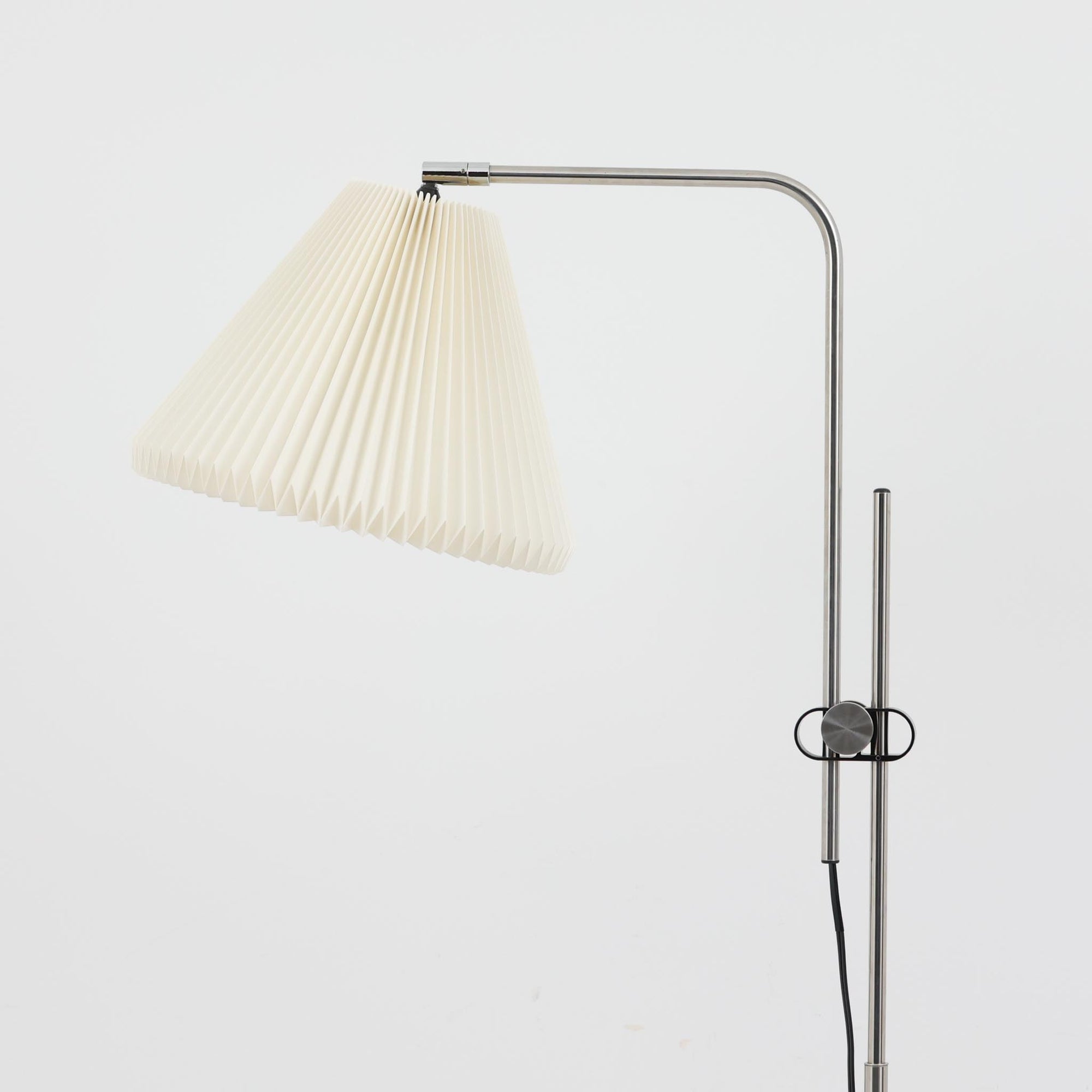 Michael Bang（マイケル・バン）によるデザインで、Le Klint（レ・クリント）から発表されたフロアランプModel 321です。高さ131cmのスチール製フレームは、無駄のない直線的なフォルムと精巧なディテールが際立ち、モダンな空間に調和します。特徴的なスライド機構によりランプの高さを調整でき、読書灯から間接照明まで幅広い用途に対応。ハンドクラフトによるプリーツシェードは柔らかい光を生み出し、北欧ビンテージならではの温もりと機能美を感じさせます。