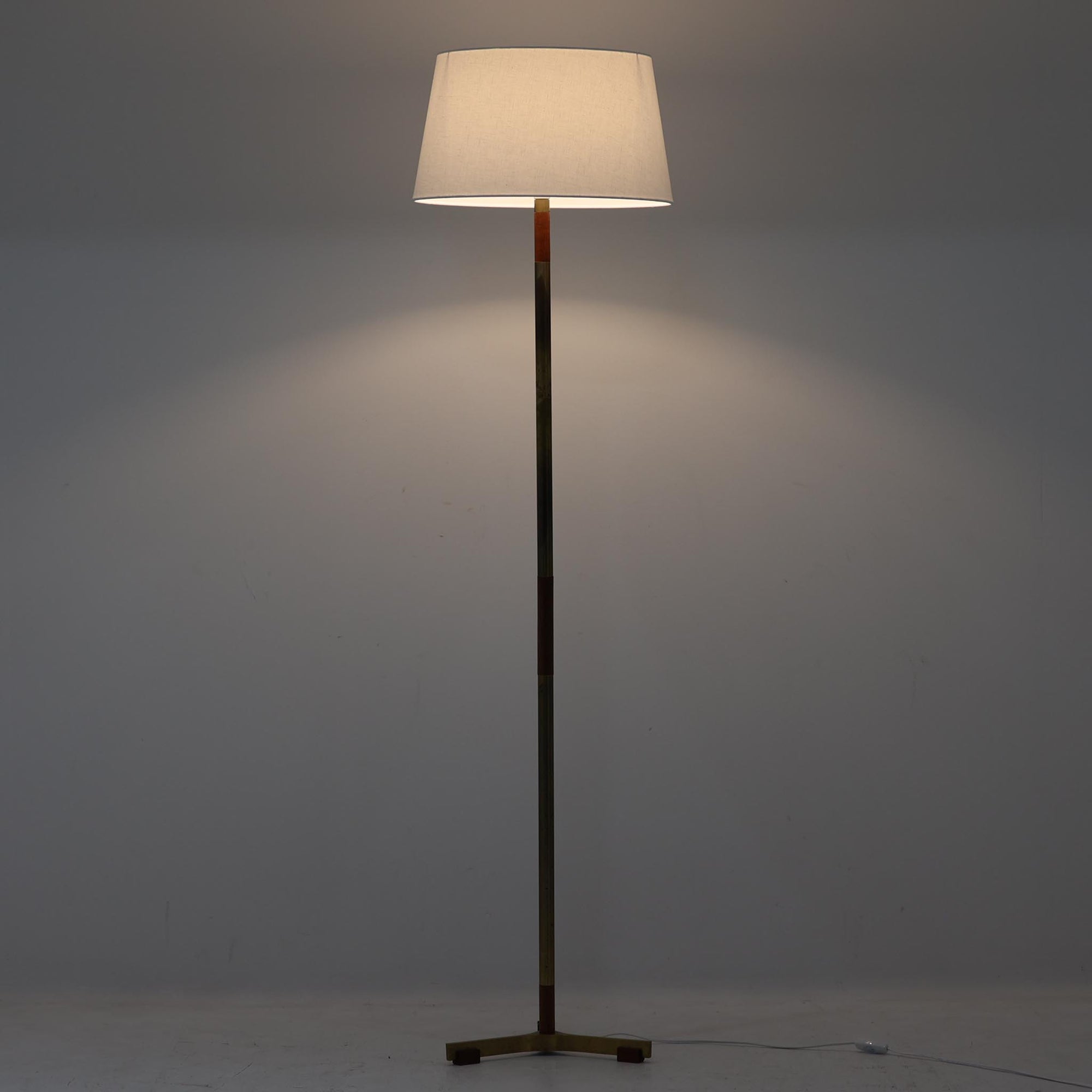 Jo HammerborgがFog & Morupのために手がけた「Monolit」は、真鍮のシャフトにチーク材のアクセントを加えたミニマルで洗練されたフロアランプです。高さ164cmの堂々たるプロポーションに、Y字型の真鍮ベースが独自の存在感を放ち、リネンシェードを通した柔らかな光が空間に落ち着きを与えます。素材のコントラストと構造美が際立つ一台は、北欧ビンテージ照明の中でも特に希少な逸品といえるでしょう。