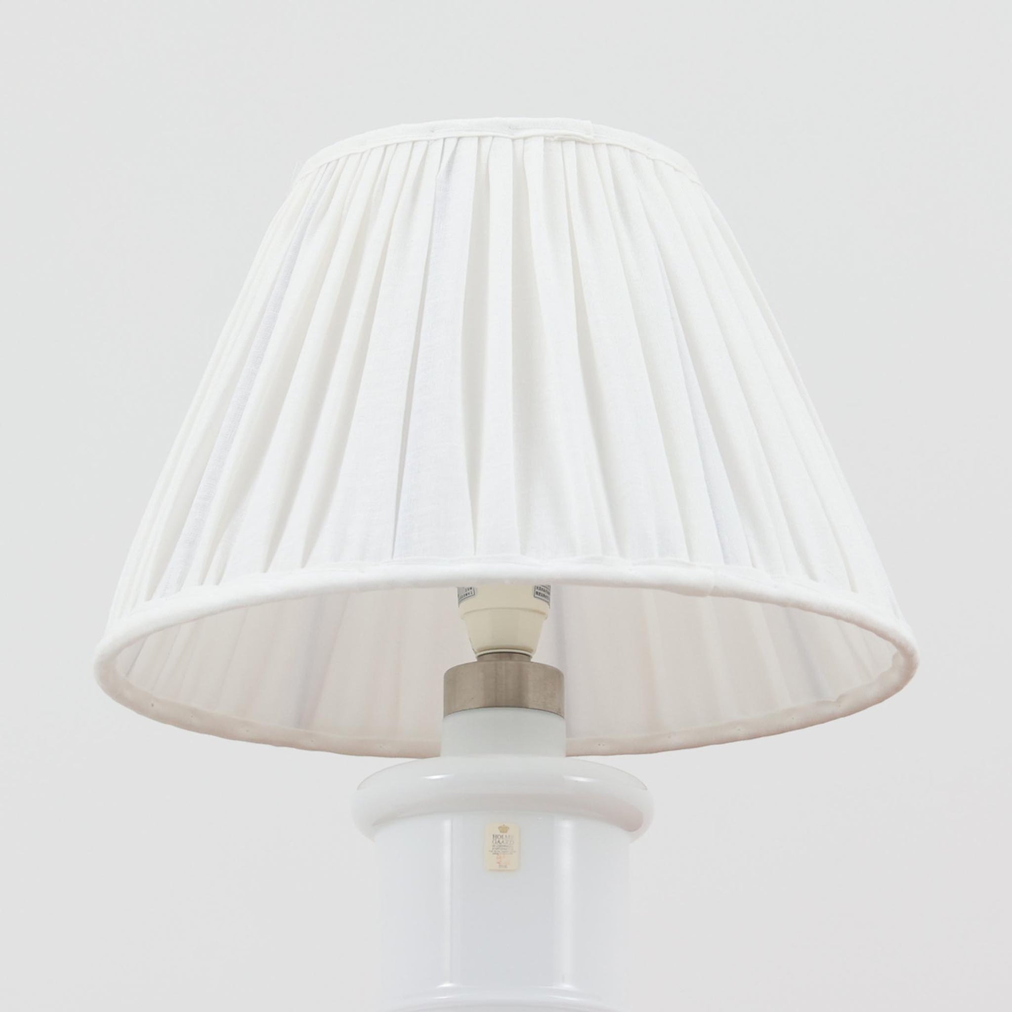 Sidse Wernerがデザインし、Holmegaard社より製造された「Apoteker」テーブルランプは、高さ46cmの堂々としたサイズ感と、白色ガラスの透明感が魅力の一品です。シリンダー状のフォルムにさりげなく入ったライン装飾が、シンプルながらも奥行きを感じさせるデザインとなっています。ガラス特有の柔らかな光の反射とリネンシェードを透過する穏やかな灯りは、リビングや寝室に落ち着いた雰囲気をもたらします。北欧ビンテージならではの洗練された存在感を楽しめる逸品です。