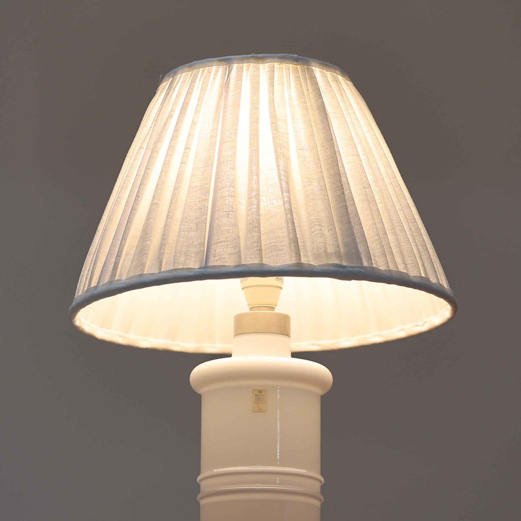 Sidse Wernerがデザインし、Holmegaard社より製造された「Apoteker」テーブルランプは、高さ46cmの堂々としたサイズ感と、白色ガラスの透明感が魅力の一品です。シリンダー状のフォルムにさりげなく入ったライン装飾が、シンプルながらも奥行きを感じさせるデザインとなっています。ガラス特有の柔らかな光の反射とリネンシェードを透過する穏やかな灯りは、リビングや寝室に落ち着いた雰囲気をもたらします。北欧ビンテージならではの洗練された存在感を楽しめる逸品です。