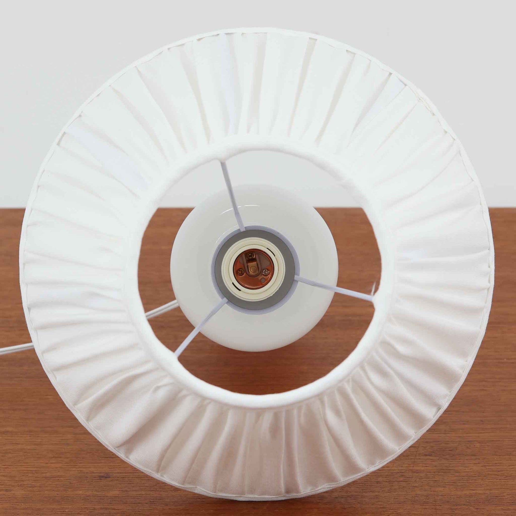 Sidse Wernerがデザインし、Holmegaard社より製造された「Apoteker」テーブルランプは、高さ46cmの堂々としたサイズ感と、白色ガラスの透明感が魅力の一品です。シリンダー状のフォルムにさりげなく入ったライン装飾が、シンプルながらも奥行きを感じさせるデザインとなっています。ガラス特有の柔らかな光の反射とリネンシェードを透過する穏やかな灯りは、リビングや寝室に落ち着いた雰囲気をもたらします。北欧ビンテージならではの洗練された存在感を楽しめる逸品です。