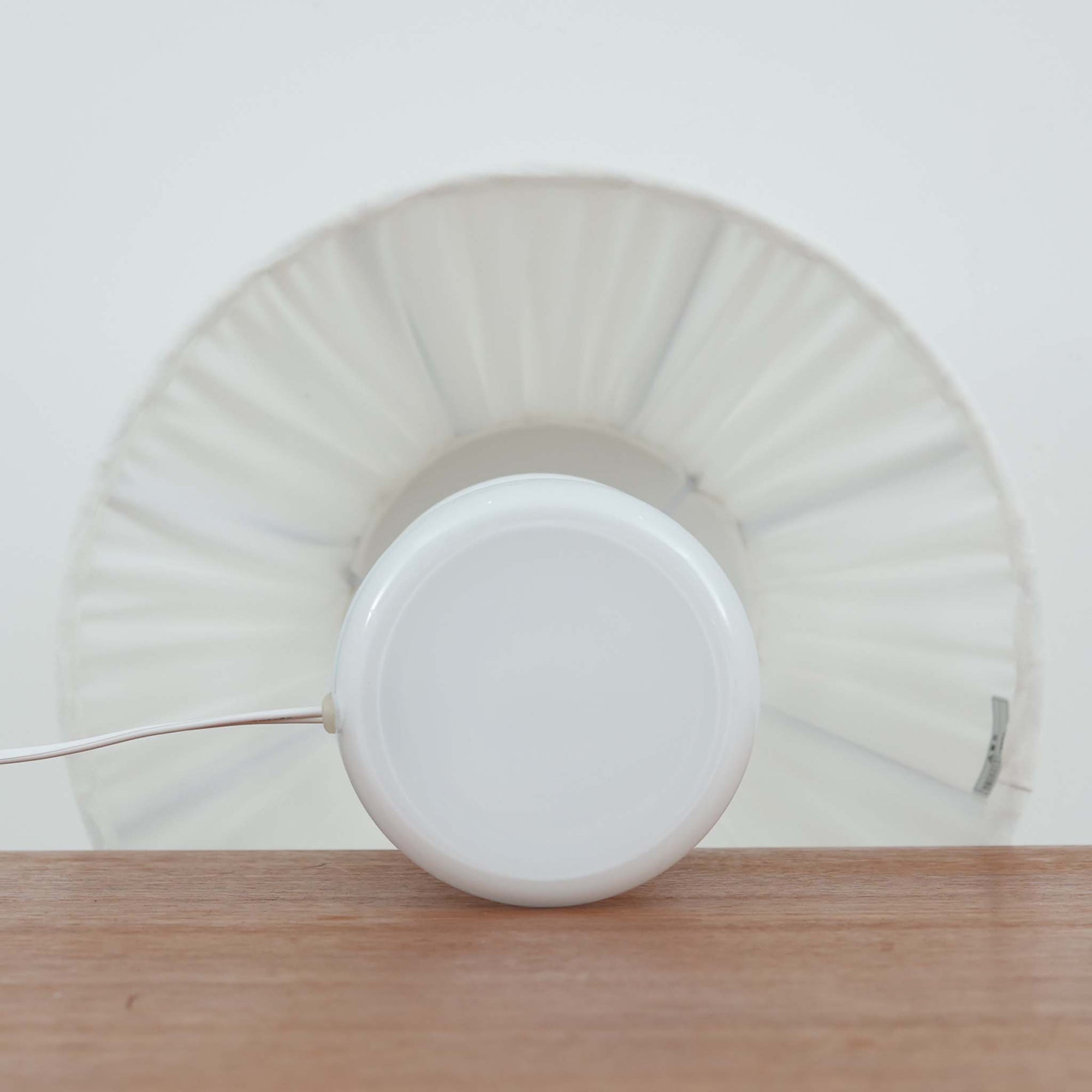 Sidse Wernerがデザインし、Holmegaard社より製造された「Apoteker」テーブルランプは、高さ46cmの堂々としたサイズ感と、白色ガラスの透明感が魅力の一品です。シリンダー状のフォルムにさりげなく入ったライン装飾が、シンプルながらも奥行きを感じさせるデザインとなっています。ガラス特有の柔らかな光の反射とリネンシェードを透過する穏やかな灯りは、リビングや寝室に落ち着いた雰囲気をもたらします。北欧ビンテージならではの洗練された存在感を楽しめる逸品です。