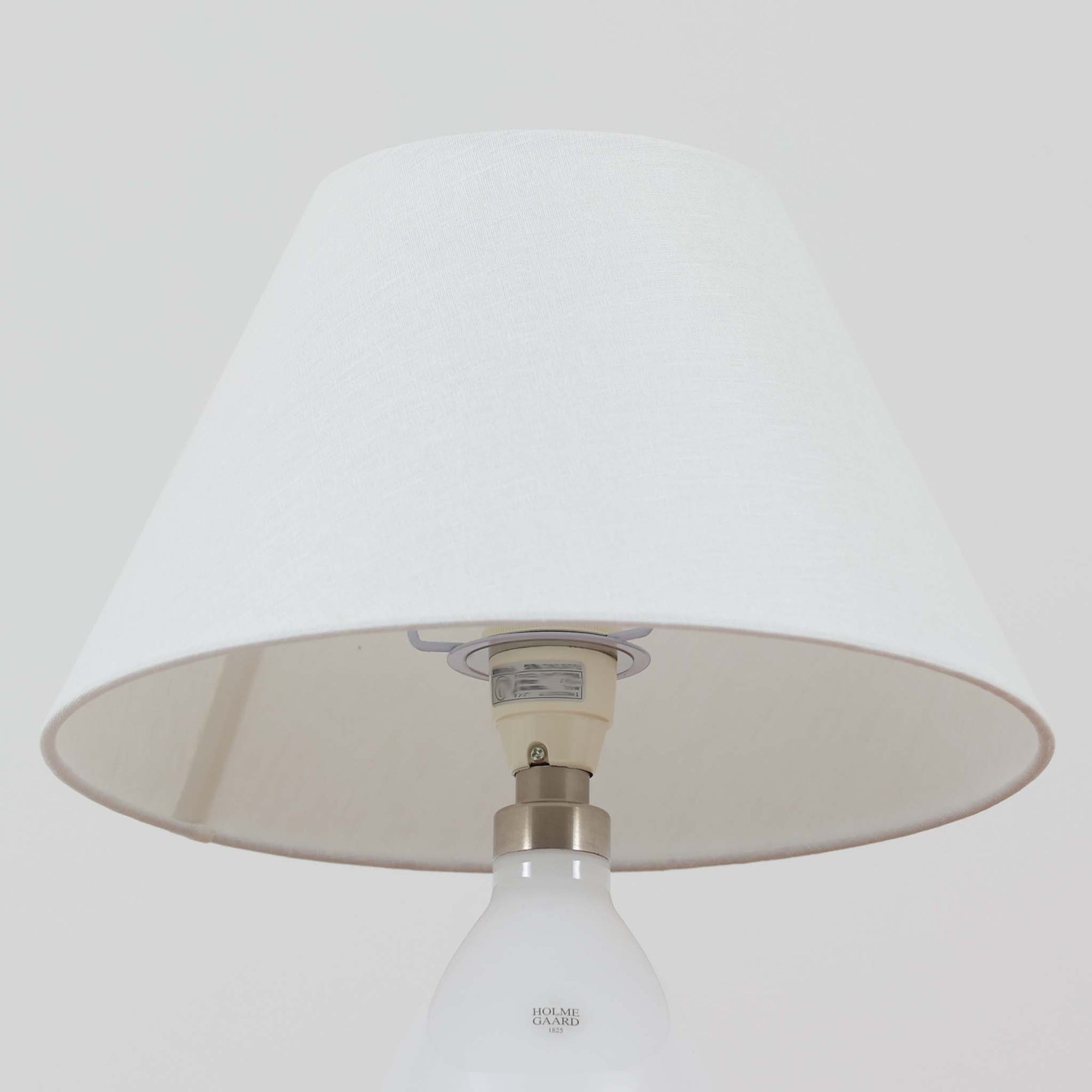 デンマークの老舗ガラスメーカー、Holmegaard（ホルムガード）社による「Cocoon」モデルのテーブルランプです。デザイナーはPeter Svarrer（ピーター・スヴァレ）で、彼らしい滑らかな曲線と透明感のあるフォルムが美しく表現されています。乳白色のガラスベースは光をやわらかく反射し、リネンシェードを通して穏やかな灯りを広げます。北欧らしいミニマルで洗練されたデザインは、ベッドサイドやリビングなどに上質な雰囲気をもたらしてくれます。