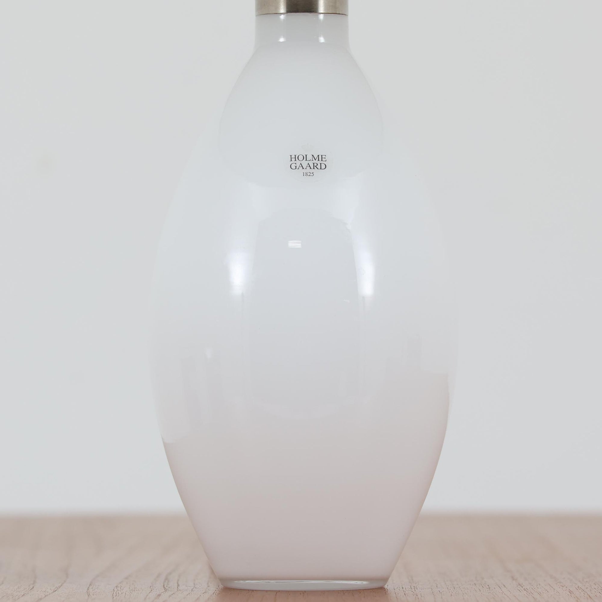 デンマークの老舗ガラスメーカー、Holmegaard（ホルムガード）社による「Cocoon」モデルのテーブルランプです。デザイナーはPeter Svarrer（ピーター・スヴァレ）で、彼らしい滑らかな曲線と透明感のあるフォルムが美しく表現されています。乳白色のガラスベースは光をやわらかく反射し、リネンシェードを通して穏やかな灯りを広げます。北欧らしいミニマルで洗練されたデザインは、ベッドサイドやリビングなどに上質な雰囲気をもたらしてくれます。