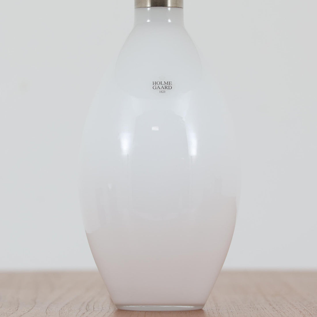 デンマークの老舗ガラスメーカー、Holmegaard（ホルムガード）社による「Cocoon」モデルのテーブルランプです。デザイナーはPeter Svarrer（ピーター・スヴァレ）で、彼らしい滑らかな曲線と透明感のあるフォルムが美しく表現されています。乳白色のガラスベースは光をやわらかく反射し、リネンシェードを通して穏やかな灯りを広げます。北欧らしいミニマルで洗練されたデザインは、ベッドサイドやリビングなどに上質な雰囲気をもたらしてくれます。