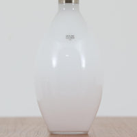 デンマークの老舗ガラスメーカー、Holmegaard（ホルムガード）社による「Cocoon」モデルのテーブルランプです。デザイナーはPeter Svarrer（ピーター・スヴァレ）で、彼らしい滑らかな曲線と透明感のあるフォルムが美しく表現されています。乳白色のガラスベースは光をやわらかく反射し、リネンシェードを通して穏やかな灯りを広げます。北欧らしいミニマルで洗練されたデザインは、ベッドサイドやリビングなどに上質な雰囲気をもたらしてくれます。