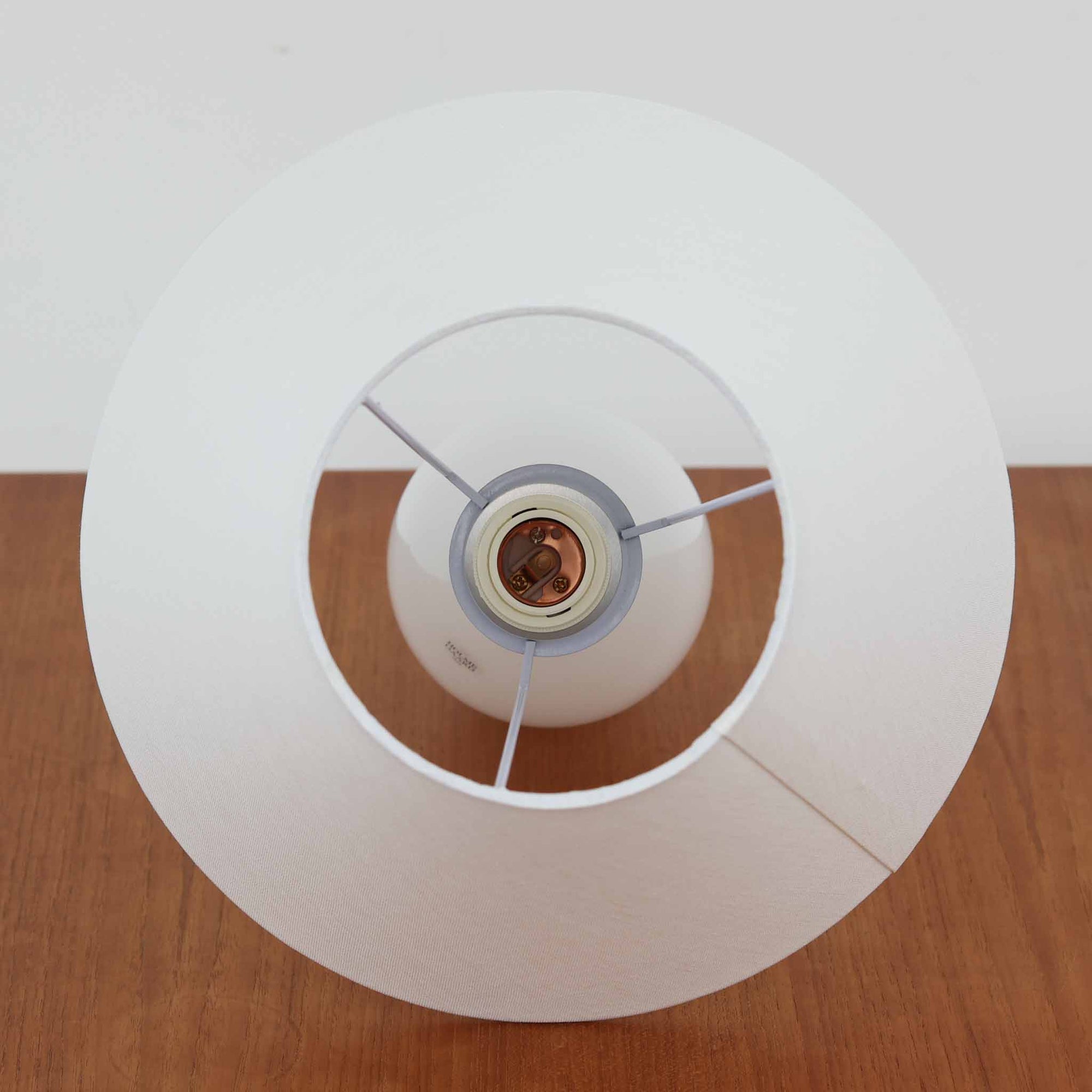 デンマークの老舗ガラスメーカー、Holmegaard（ホルムガード）社による「Cocoon」モデルのテーブルランプです。デザイナーはPeter Svarrer（ピーター・スヴァレ）で、彼らしい滑らかな曲線と透明感のあるフォルムが美しく表現されています。乳白色のガラスベースは光をやわらかく反射し、リネンシェードを通して穏やかな灯りを広げます。北欧らしいミニマルで洗練されたデザインは、ベッドサイドやリビングなどに上質な雰囲気をもたらしてくれます。