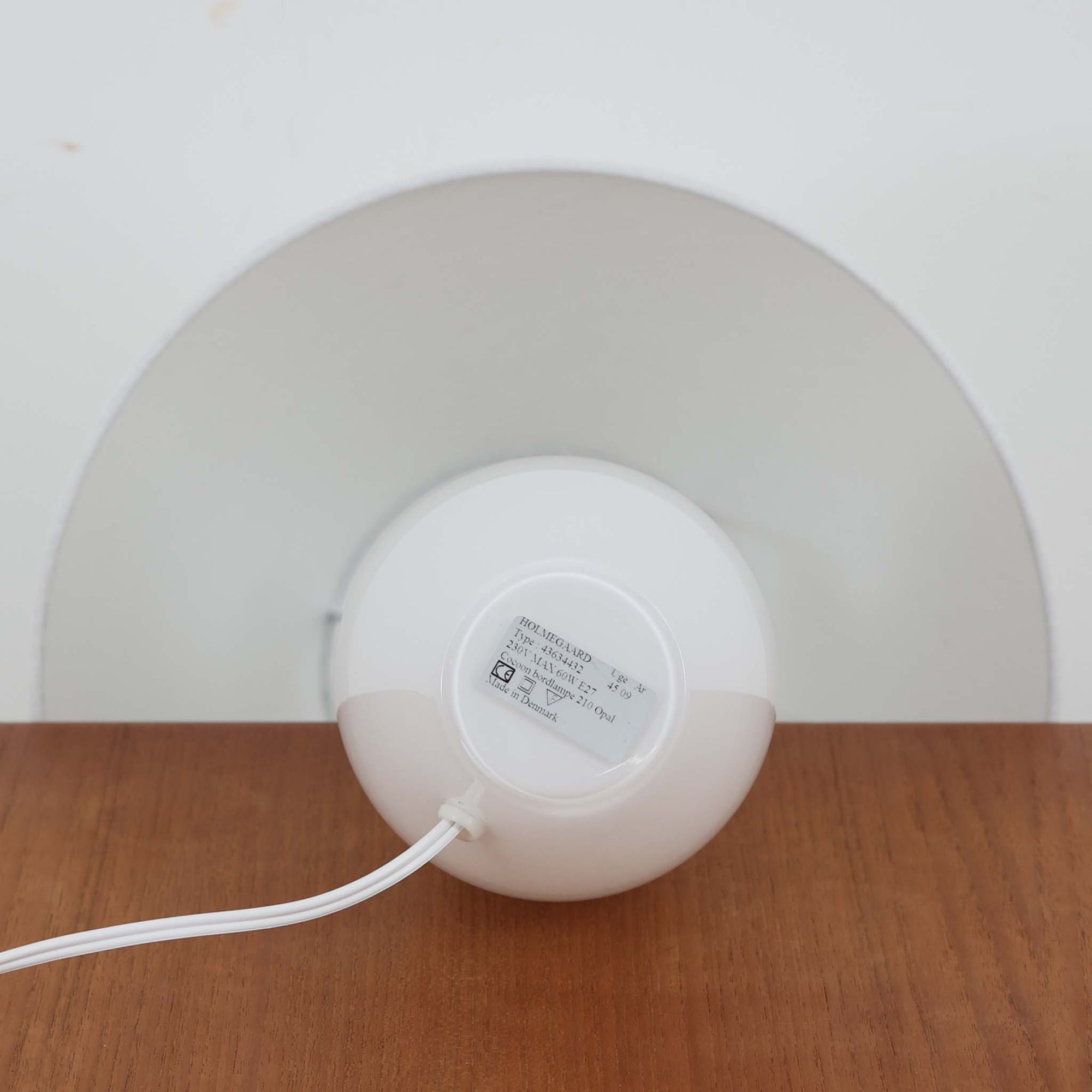 デンマークの老舗ガラスメーカー、Holmegaard（ホルムガード）社による「Cocoon」モデルのテーブルランプです。デザイナーはPeter Svarrer（ピーター・スヴァレ）で、彼らしい滑らかな曲線と透明感のあるフォルムが美しく表現されています。乳白色のガラスベースは光をやわらかく反射し、リネンシェードを通して穏やかな灯りを広げます。北欧らしいミニマルで洗練されたデザインは、ベッドサイドやリビングなどに上質な雰囲気をもたらしてくれます。