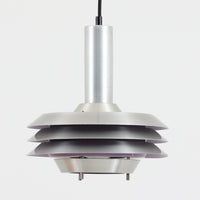 Carl Thoreがデザインし、Granhaga社より発表された直径28cmのペンダントライトです。アルミ製のシェードを幾重にも重ねた構造が特徴で、点灯すると隙間から柔らかな光が漏れ、独特の陰影と奥行きを生み出します。外側はシルバー、内側には紫がかった色味が施され、消灯時と点灯時で異なる表情を楽しめます。モダンでありながら温かみのある北欧らしい光のデザインは、ダイニングやリビングの照明として空間にアクセントを与えます。ビンテージならではの存在感を放つ希少な一品です。