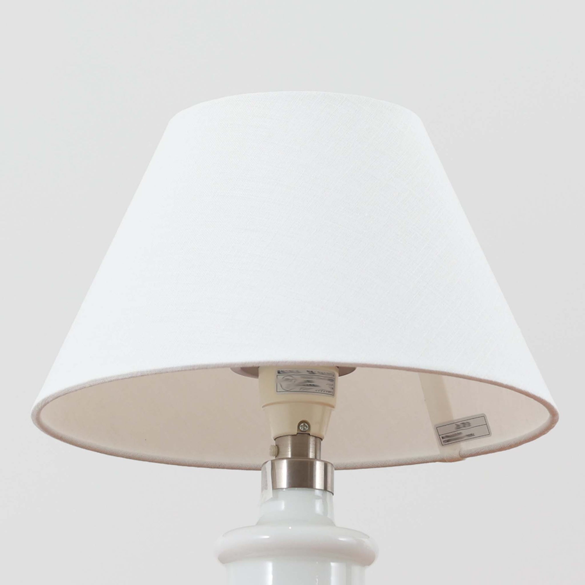 Sidse Werner（シセ・ヴェルナー）がデザインし、Holmegaard（ホルムガード）より製造されたテーブルランプ「Apoteker」です。高さ29cmと小ぶりなサイズで、艶やかなホワイトガラスのベースが柔らかな印象を与えます。リネンシェードを通した光は優しく拡散し、ナチュラルな雰囲気を演出。シンプルでありながら彫刻的なフォルムが存在感を放ち、ベッドサイドやデスク、リビングのサイドテーブルなど様々な空間で活躍します。北欧デザインの温もりを感じられるビンテージ照明です。