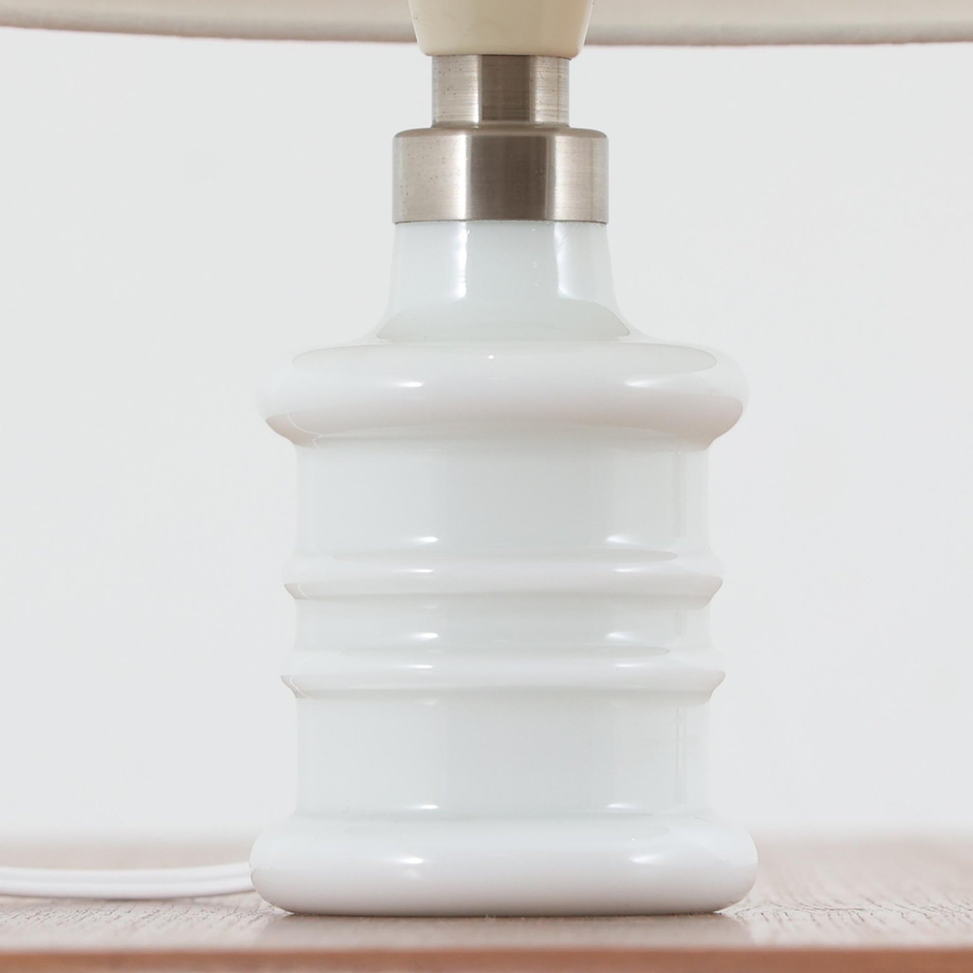 Sidse Werner（シセ・ヴェルナー）がデザインし、Holmegaard（ホルムガード）より製造されたテーブルランプ「Apoteker」です。高さ29cmと小ぶりなサイズで、艶やかなホワイトガラスのベースが柔らかな印象を与えます。リネンシェードを通した光は優しく拡散し、ナチュラルな雰囲気を演出。シンプルでありながら彫刻的なフォルムが存在感を放ち、ベッドサイドやデスク、リビングのサイドテーブルなど様々な空間で活躍します。北欧デザインの温もりを感じられるビンテージ照明です。