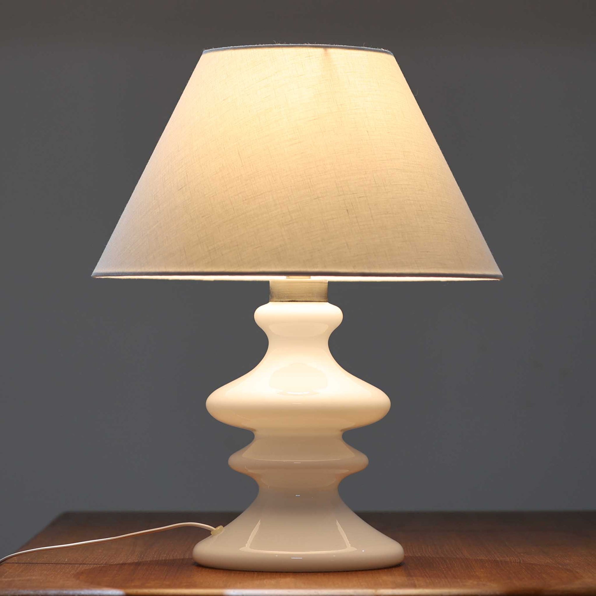 Per Lutken（ペア・ルッケン）によるデザイン、Holmegaard（ホルムガード）製のテーブルランプ「Mary」です。高さ44cmの存在感あるサイズで、滑らかな曲線を描くホワイトガラスのベースは柔らかい光沢を放ち、北欧らしい洗練された印象を与えます。シンプルなリネンシェードを通した光は温かみのある雰囲気を演出し、リビングやベッドサイドに心地よい灯りを添えます。北欧モダンデザインの魅力と職人技が息づくビンテージ照明です。