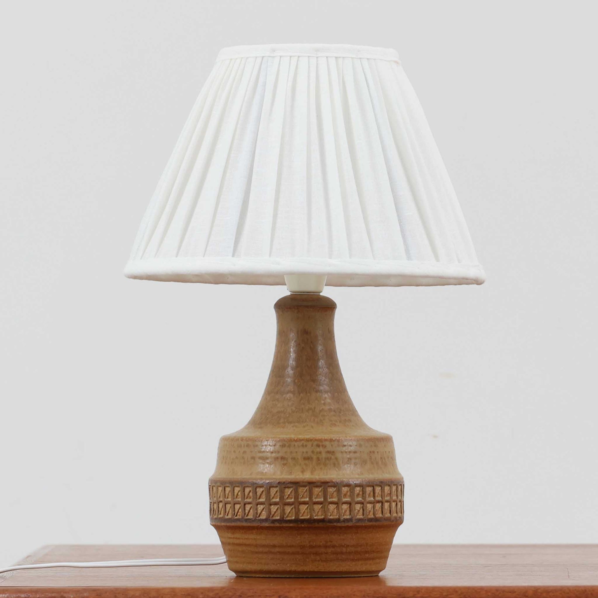 Soholm Keramik（スーホルム・セラミック）製のテーブルランプです。落ち着いたブラウンの陶磁器ボディに幾何学模様の装飾が施され、シンプルながらも存在感のあるデザインが魅力です。高さ39cmと扱いやすいサイズ感で、リビングや寝室のサイドテーブルに心地よい灯りを添えてくれます。北欧ビンテージならではの温かみある質感が、空間に柔らかな雰囲気をもたらします。