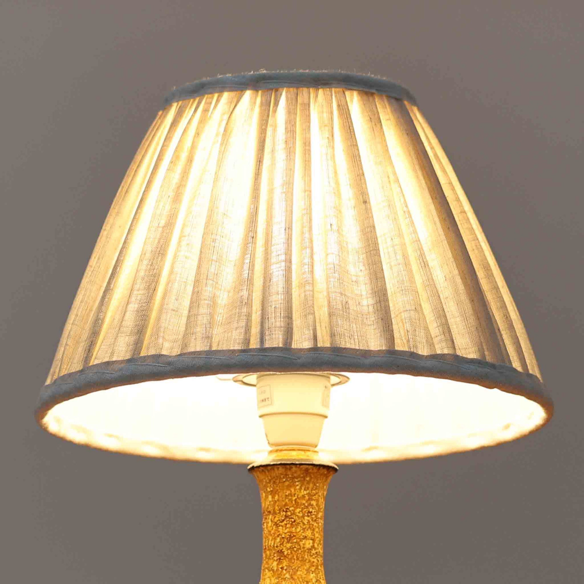 デンマークの陶芸家 Jette Helleroe（イェッテ・ヘレロー）によるテーブルランプです。素朴な質感と温かみのある釉薬のグラデーションが魅力で、ベースには深みのあるブラウンとオレンジを基調とした幾何学的な模様が施されています。手仕事ならではの味わいが感じられ、点灯時にはやわらかな灯りが陶器の表情をより一層引き立てます。ナチュラルなリネンシェードとの組み合わせが優しく、北欧らしい落ち着いた雰囲気を空間にもたらします。