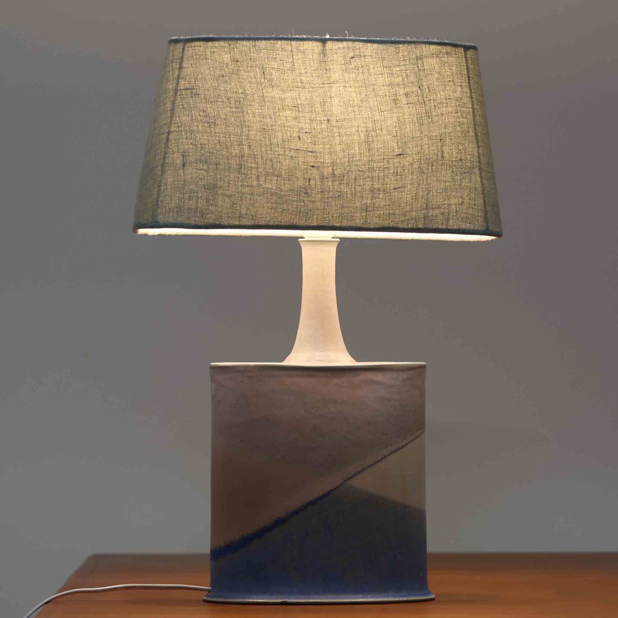こちらのテーブルランプは、陶磁器ベースに淡いパープルやブルーを溶け合わせたような独特の釉薬表情が魅力で、ビンテージならではの柔らかなグラデーションが優しい存在感を放つ一品です。細く立ち上がる支柱にリネンシェードを組み合わせたシンプルな構造は安定感があり、点灯時にはシェード越しに温かく穏やかな光が広がります。高さ46cmと扱いやすいサイズで、ベッドサイドやリビングのサイドテーブルにも取り入れやすく、北欧らしい静かな色彩と経年の味わいを楽しめるビンテージ照明です。