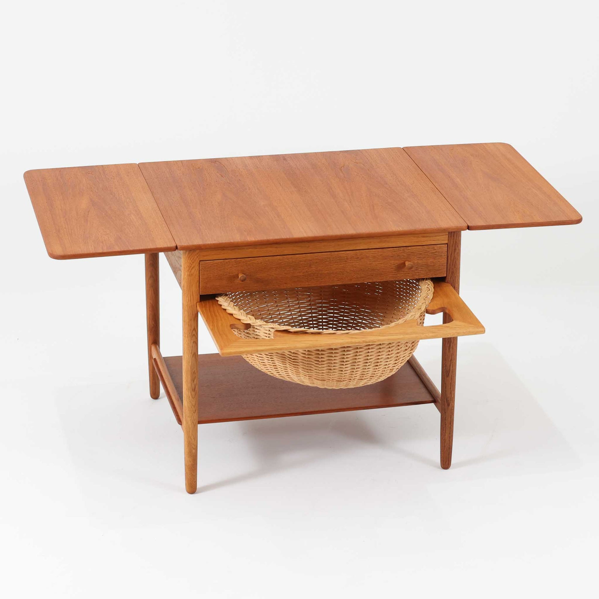 ハンス・J・ウェグナーが手がけ、Andreas Tuck社より製作されたAT33ソーイングテーブルは、天板を広げられる独創的な構造と実用性を兼ね備えた北欧ビンテージを代表する一台です。中央には引き出しと仕切り付き収納、下部にはラタンバスケットを備え、道具をすっきりと収められる設計が魅力。AT33は複数の素材構成で展開されたモデルですが、こちらは天板にチーク突板材、脚部にオーク無垢材を用いた仕様で、素材のコントラストと軽やかな佇まいが特徴です。異素材を巧みに組み合わせた構造と端正なプロポーションは、使うほどに職人技と経年変化の美しさを実感できます。