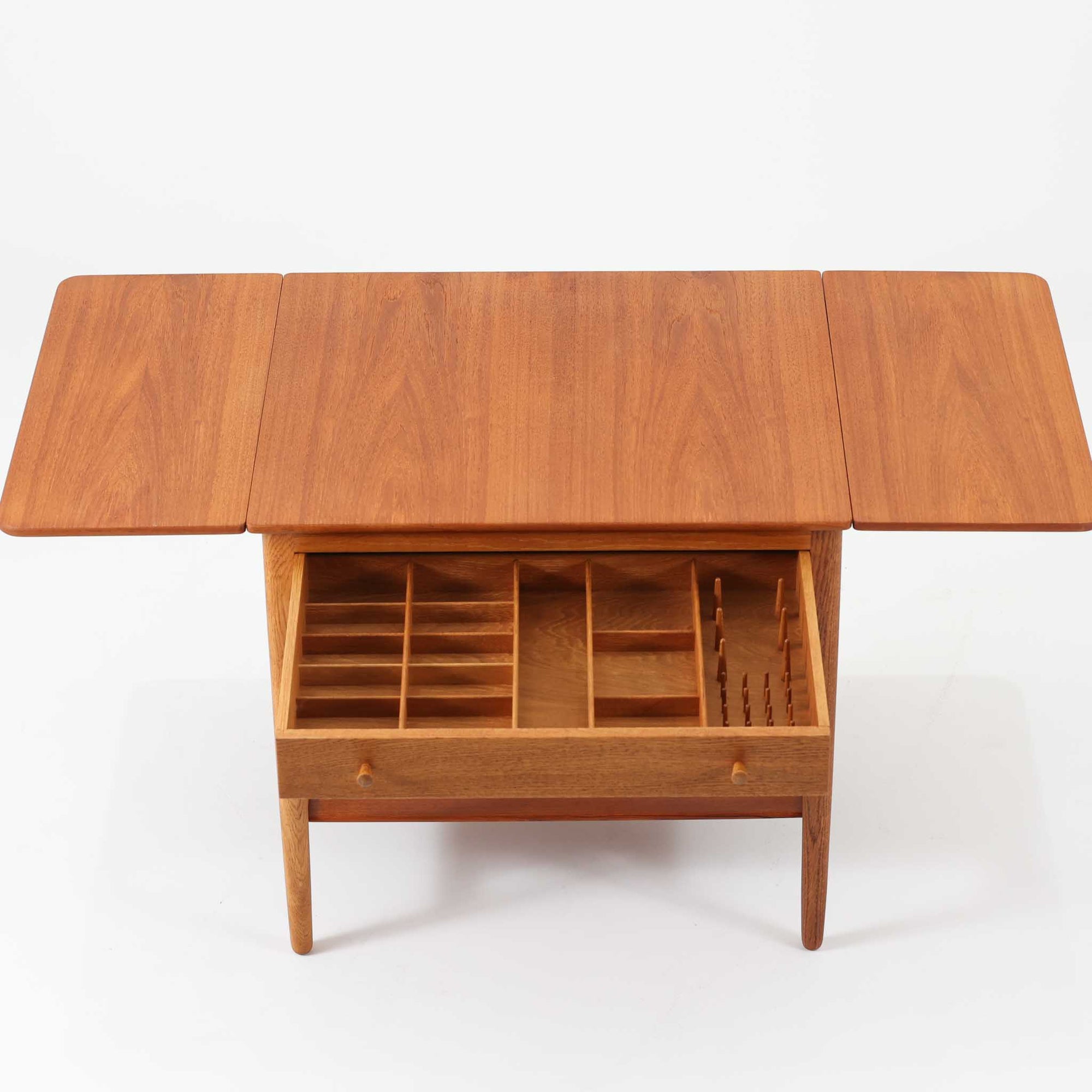 ハンス・J・ウェグナーが手がけ、Andreas Tuck社より製作されたAT33ソーイングテーブルは、天板を広げられる独創的な構造と実用性を兼ね備えた北欧ビンテージを代表する一台です。中央には引き出しと仕切り付き収納、下部にはラタンバスケットを備え、道具をすっきりと収められる設計が魅力。AT33は複数の素材構成で展開されたモデルですが、こちらは天板にチーク突板材、脚部にオーク無垢材を用いた仕様で、素材のコントラストと軽やかな佇まいが特徴です。異素材を巧みに組み合わせた構造と端正なプロポーションは、使うほどに職人技と経年変化の美しさを実感できます。