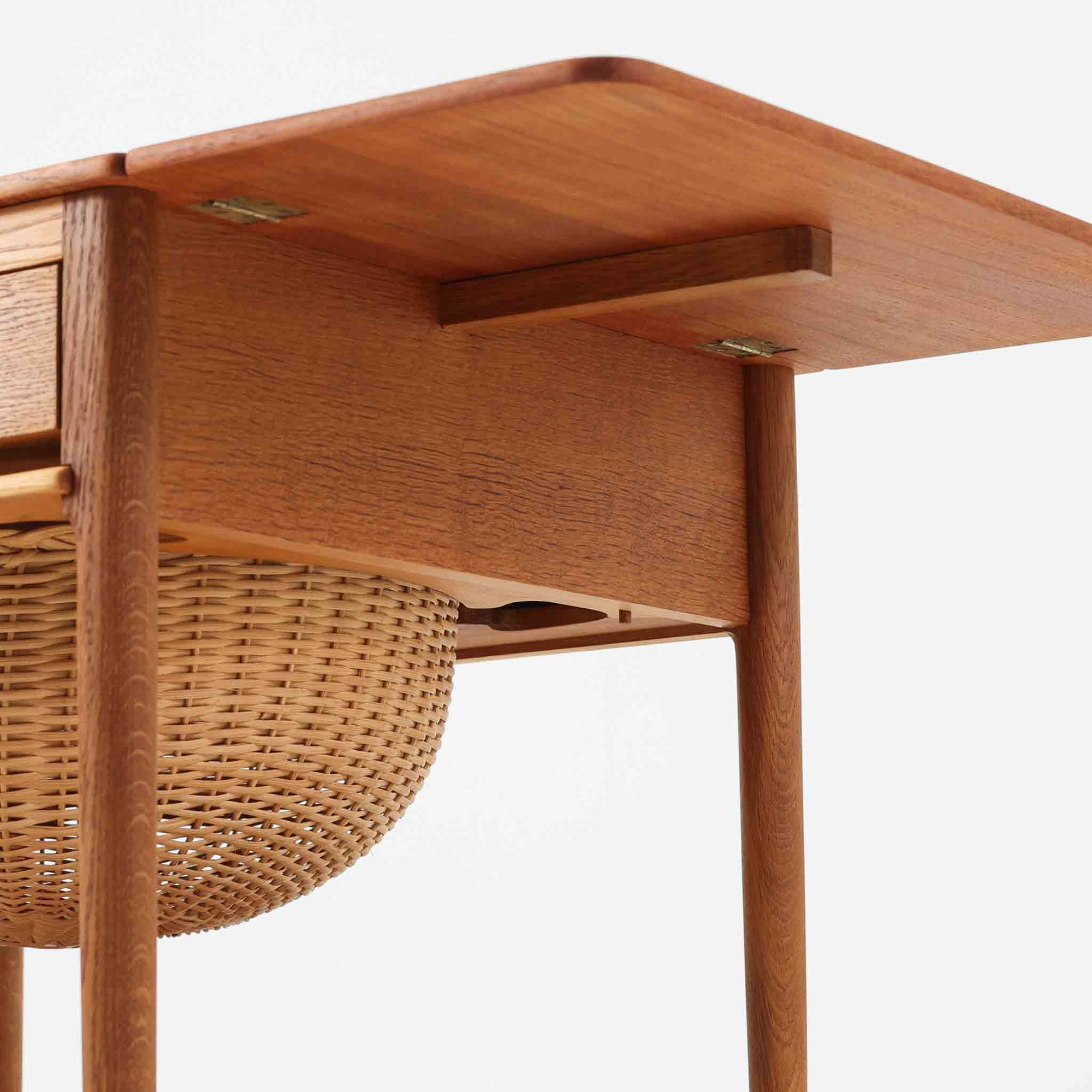 ハンス・J・ウェグナーが手がけ、Andreas Tuck社より製作されたAT33ソーイングテーブルは、天板を広げられる独創的な構造と実用性を兼ね備えた北欧ビンテージを代表する一台です。中央には引き出しと仕切り付き収納、下部にはラタンバスケットを備え、道具をすっきりと収められる設計が魅力。AT33は複数の素材構成で展開されたモデルですが、こちらは天板にチーク突板材、脚部にオーク無垢材を用いた仕様で、素材のコントラストと軽やかな佇まいが特徴です。異素材を巧みに組み合わせた構造と端正なプロポーションは、使うほどに職人技と経年変化の美しさを実感できます。