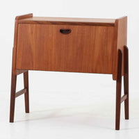 チーク材を用いた小ぶりなキャビネットは、直線を基調としつつ柔らかな丸みを持たせた側板と脚部のラインが印象的な北欧ビンテージ家具です。前板一枚で構成されたフラップ扉には掘り込み式の取っ手が設けられ、開閉時の所作も美しく、内部には実用的な収納棚を備えています。幅69cmと取り入れやすいサイズ感で、リビングや玄関、ベッドサイドの収納としても活躍し、経年により深みを増したチーク材の木目と職人技が静かな存在感を放つ一台です。