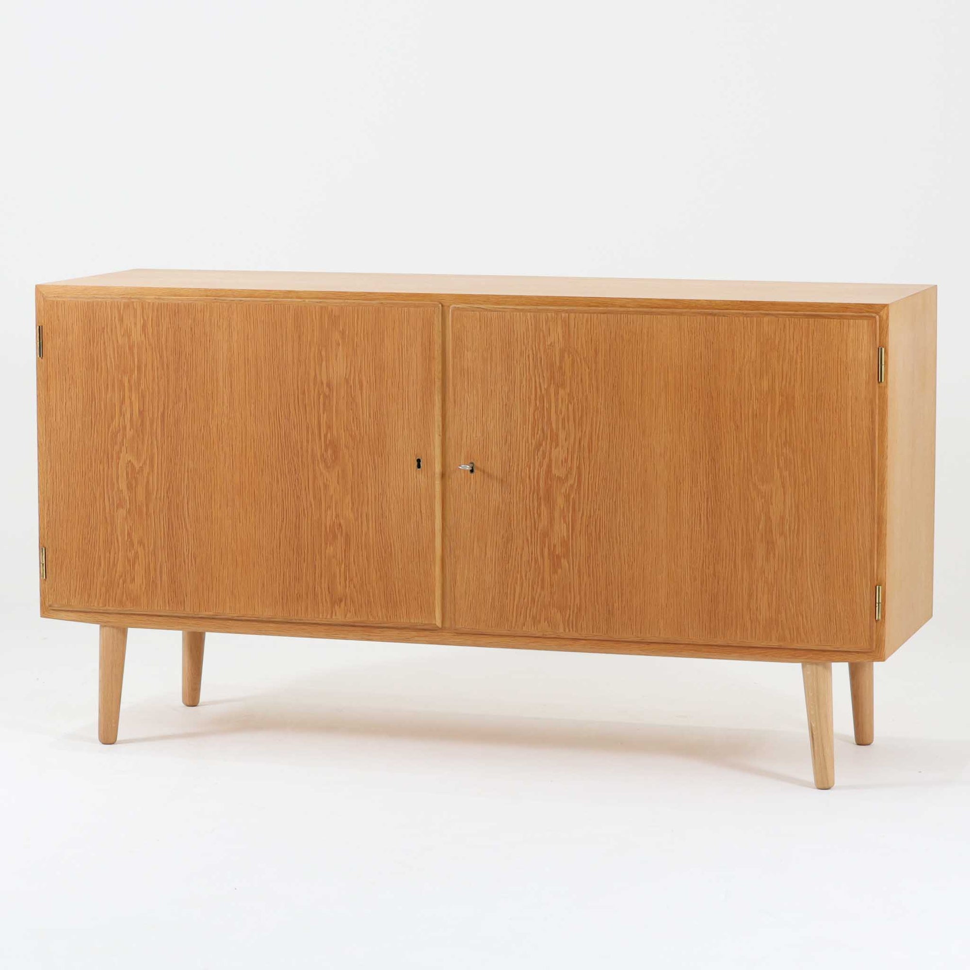 Poul Hundevadが手がけ、Hundevad & Coより製作されたキャビネットです。オーク材の端正な木目を活かしたフラットな扉構成と、細身のテーパードレッグが北欧モダンらしい軽やかさを演出します。内部は可動棚と可動式の浅型トレイを備え、書類や食器、小物まで用途に応じた整理が可能。天板下の構造や金物の収まりにも丁寧な作りが感じられ、長年の使用で深みを増した素材感がビンテージならではの魅力として空間に静かな存在感を添えます。