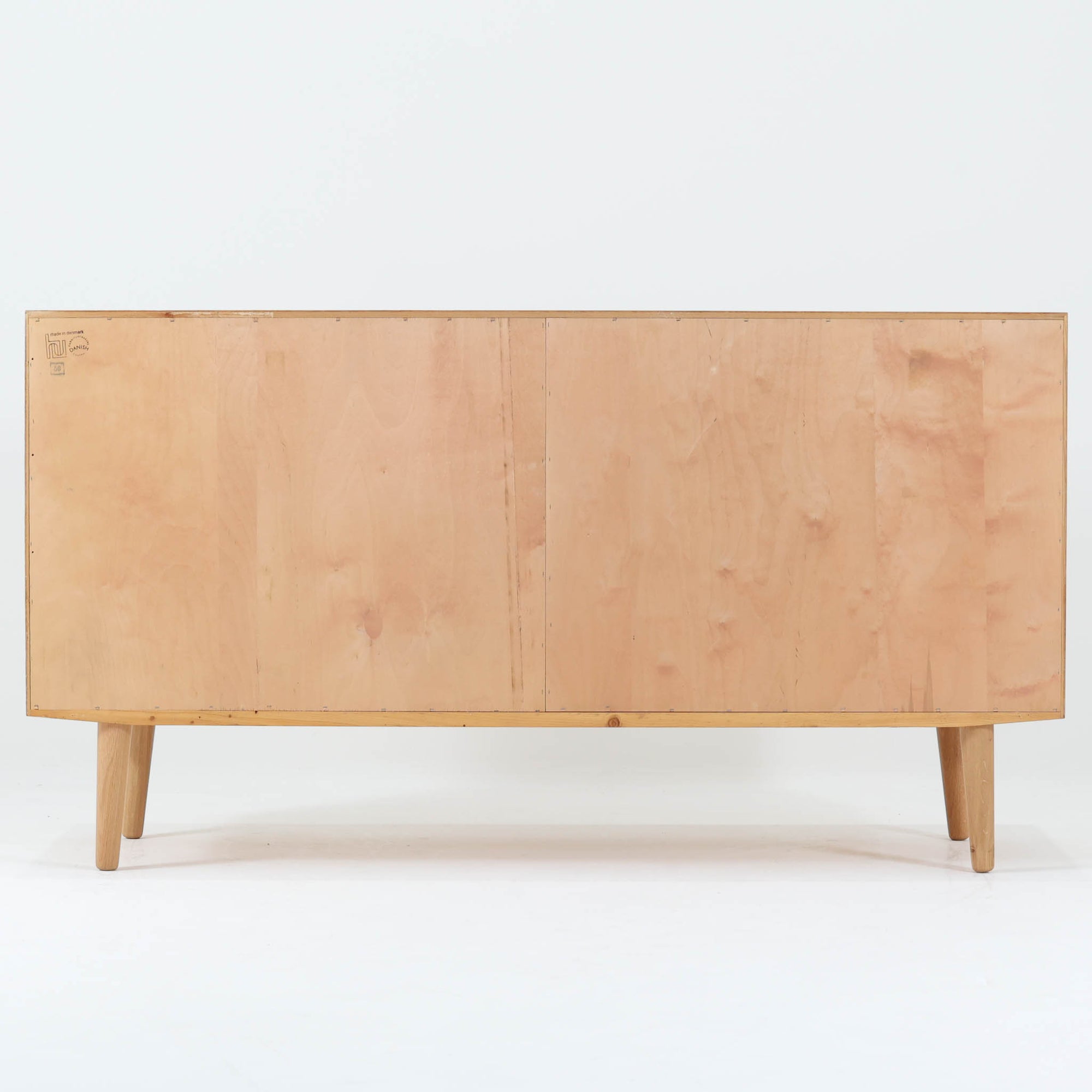 Poul Hundevadが手がけ、Hundevad &amp; Coより製作されたキャビネットです。オーク材の端正な木目を活かしたフラットな扉構成と、細身のテーパードレッグが北欧モダンらしい軽やかさを演出します。内部は可動棚と可動式の浅型トレイを備え、書類や食器、小物まで用途に応じた整理が可能。天板下の構造や金物の収まりにも丁寧な作りが感じられ、長年の使用で深みを増した素材感がビンテージならではの魅力として空間に静かな存在感を添えます。