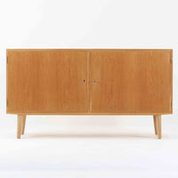 Poul Hundevadが手がけ、Hundevad & Coより製作されたキャビネットです。オーク材の端正な木目を活かしたフラットな扉構成と、細身のテーパードレッグが北欧モダンらしい軽やかさを演出します。内部は可動棚と可動式の浅型トレイを備え、書類や食器、小物まで用途に応じた整理が可能。天板下の構造や金物の収まりにも丁寧な作りが感じられ、長年の使用で深みを増した素材感がビンテージならではの魅力として空間に静かな存在感を添えます。