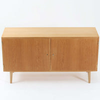 Poul Hundevadが手がけ、Hundevad & Coより製作されたキャビネットです。オーク材の端正な木目を活かしたフラットな扉構成と、細身のテーパードレッグが北欧モダンらしい軽やかさを演出します。内部は可動棚と可動式の浅型トレイを備え、書類や食器、小物まで用途に応じた整理が可能。天板下の構造や金物の収まりにも丁寧な作りが感じられ、長年の使用で深みを増した素材感がビンテージならではの魅力として空間に静かな存在感を添えます。